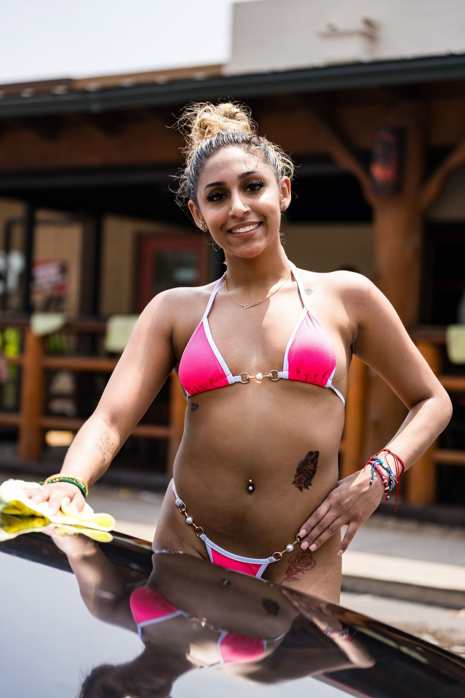 Woman in pink bikini poses confidently during outdoor car wash fundraiser.