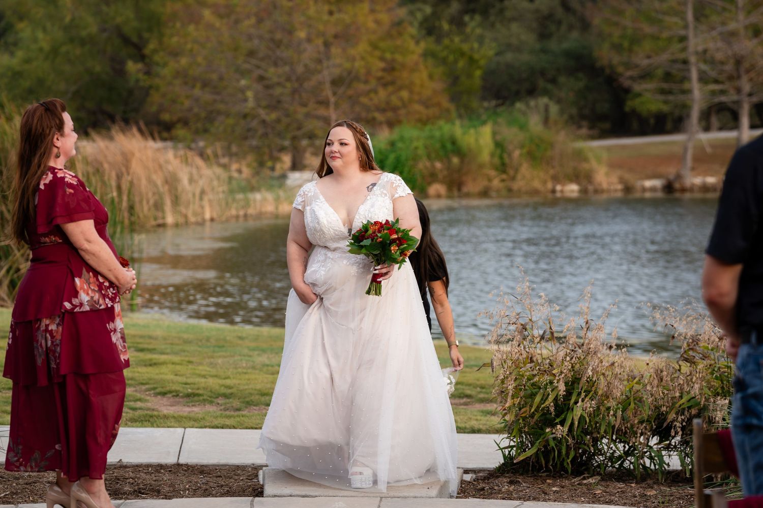 A wedding ceremony takes place near a serene pond with autumn foliage in the background.