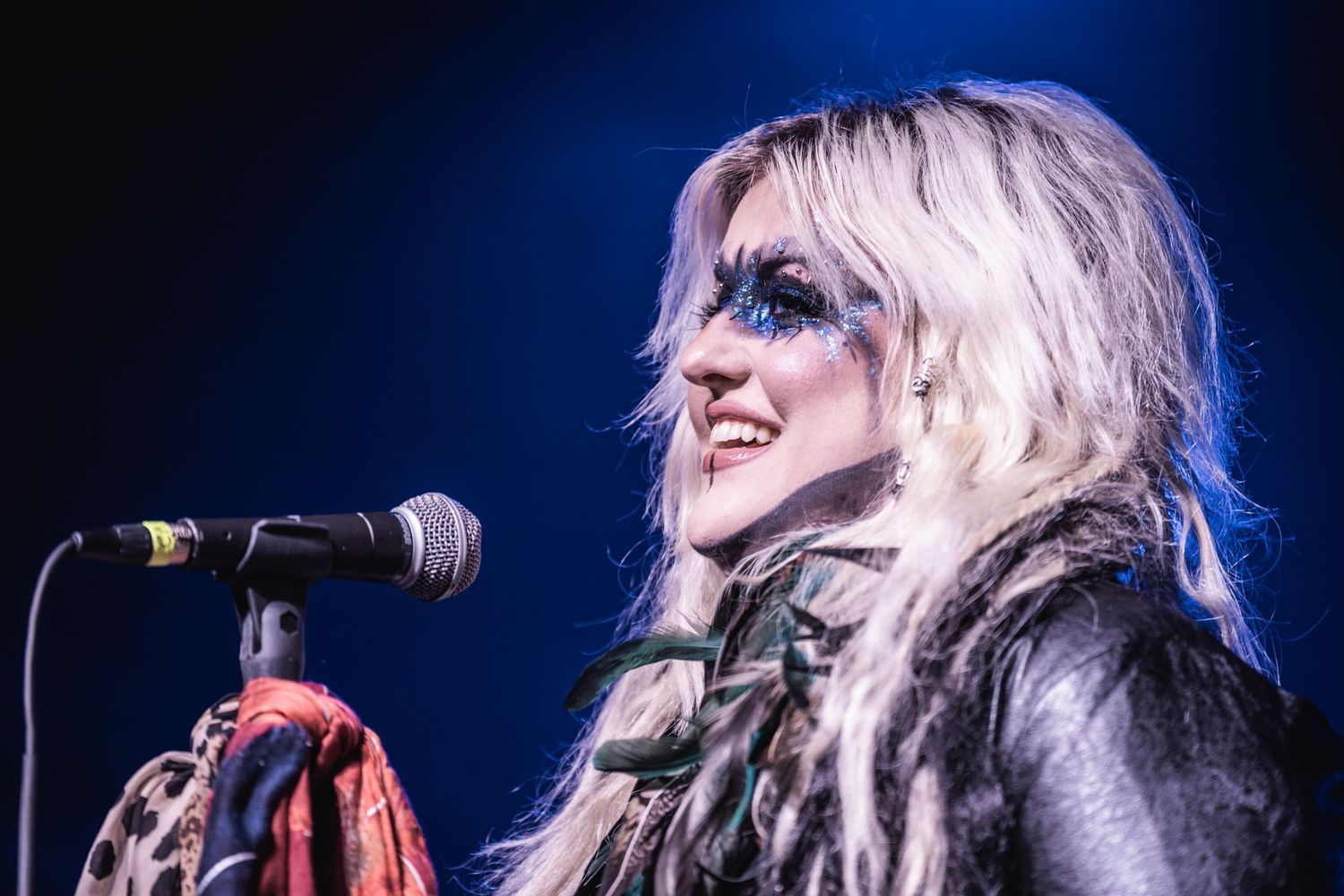 Rock performer singing into microphone with dramatic stage lighting and theatrical makeup.