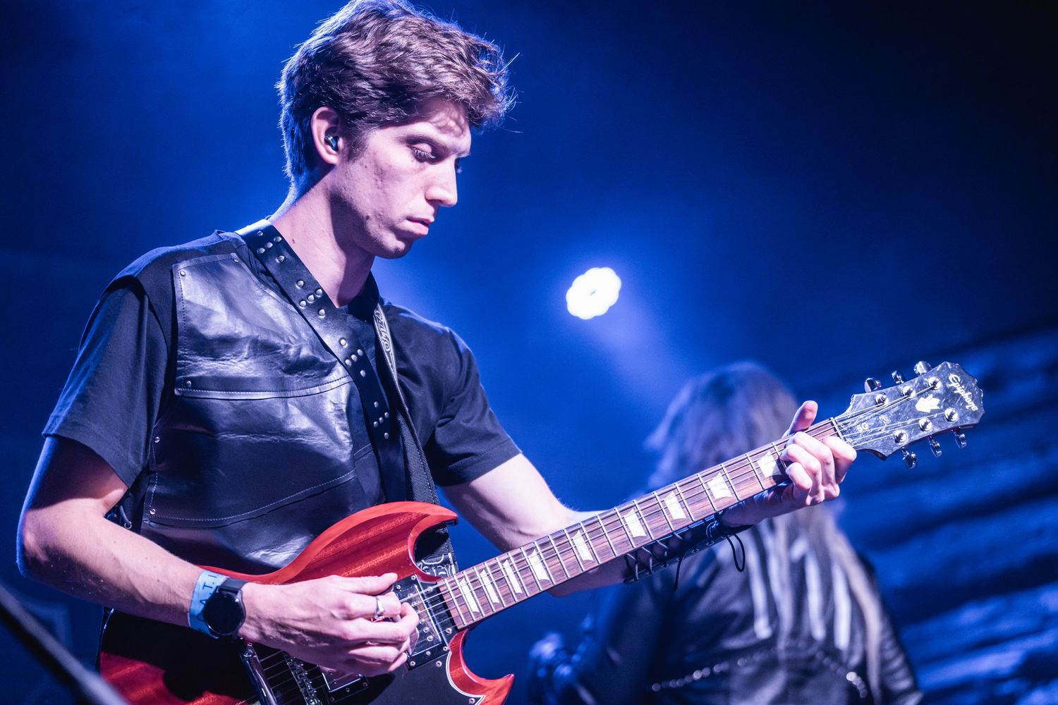 Guitarist playing red electric guitar during live performance with blue stage lighting.