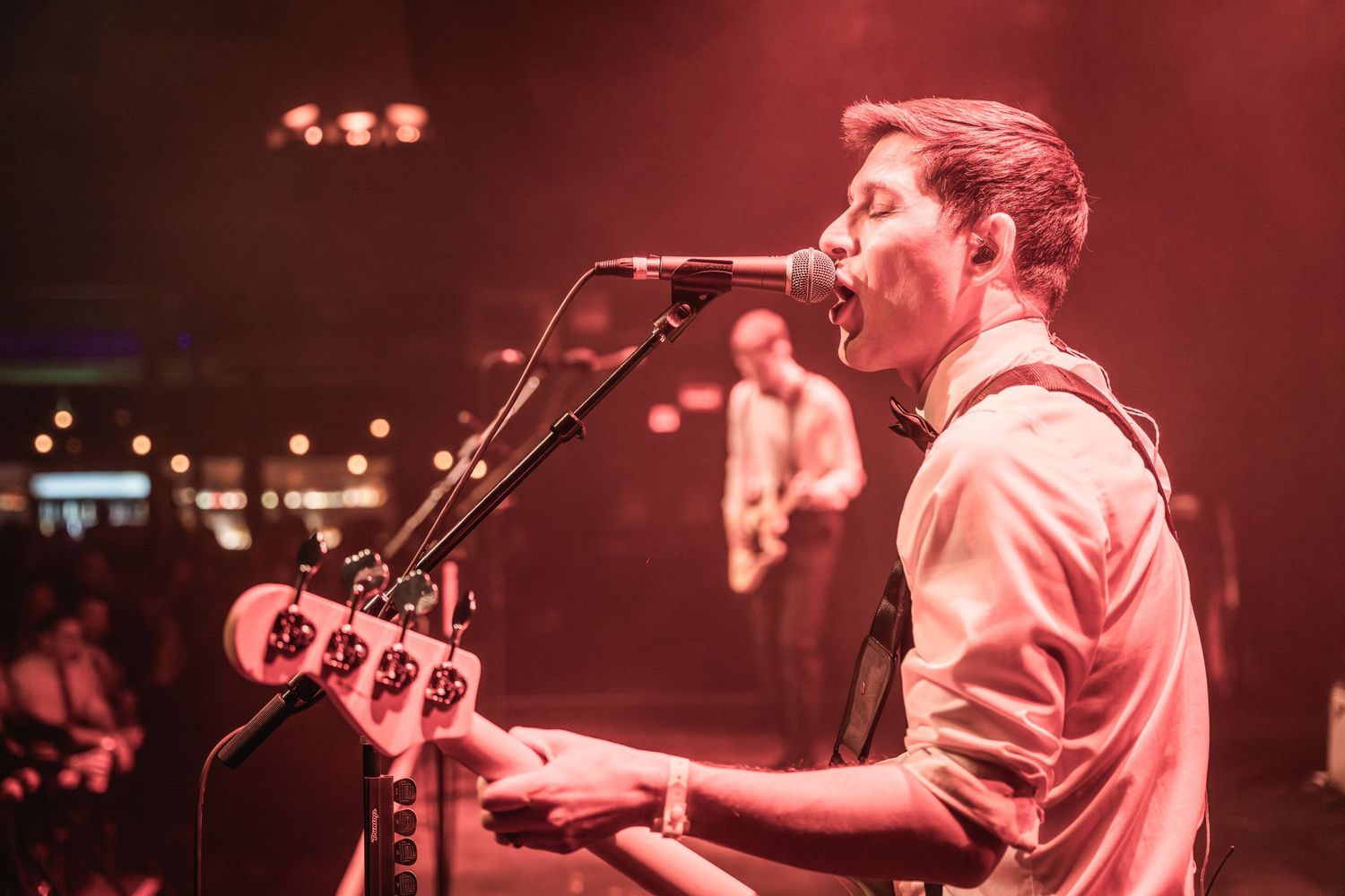 Musician performs on bass guitar under dramatic red stage lighting during live concert.