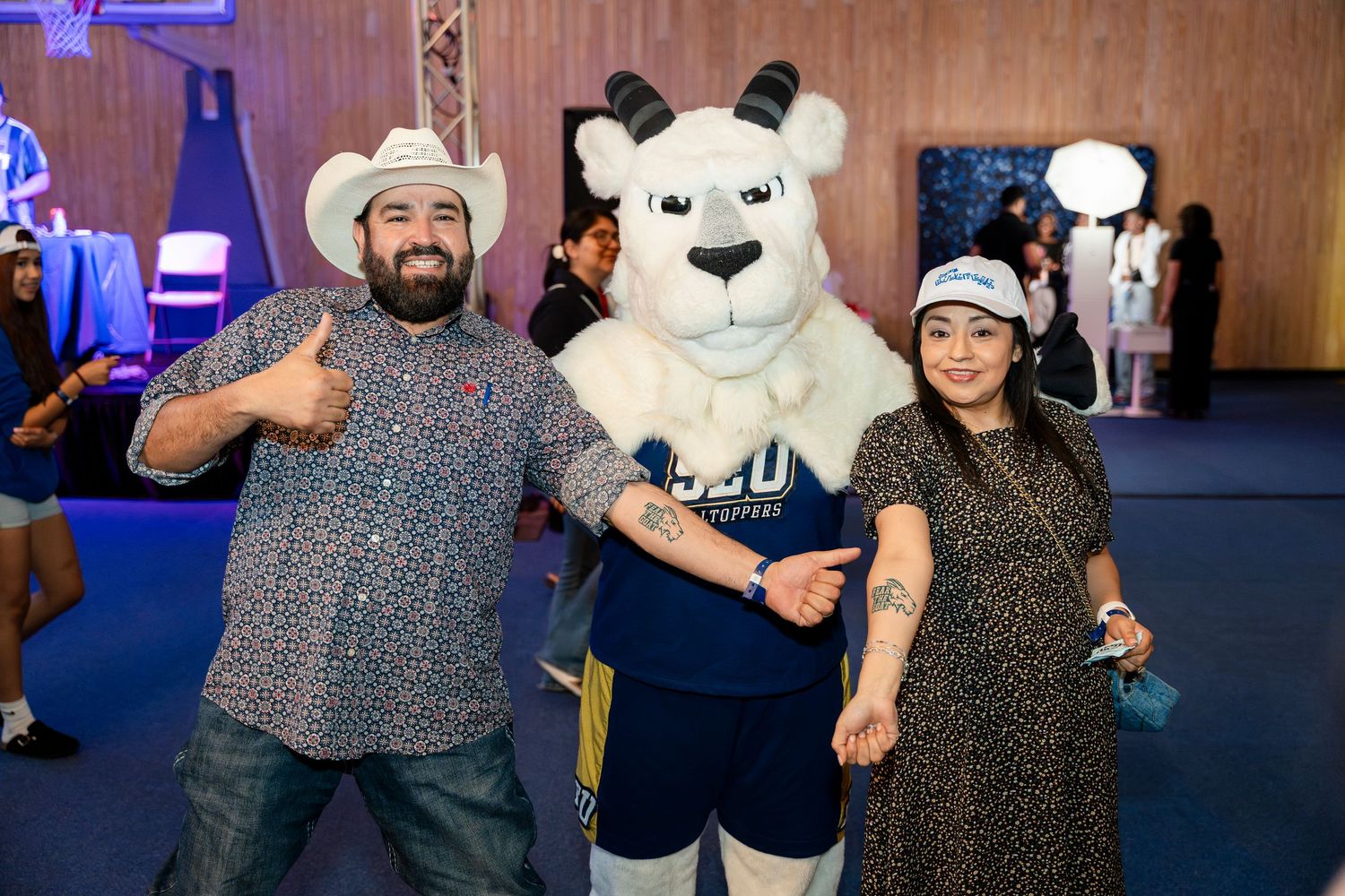 People with cowboy hats pose with a life-sized sports mascot polar bear character at an indoor event venue.