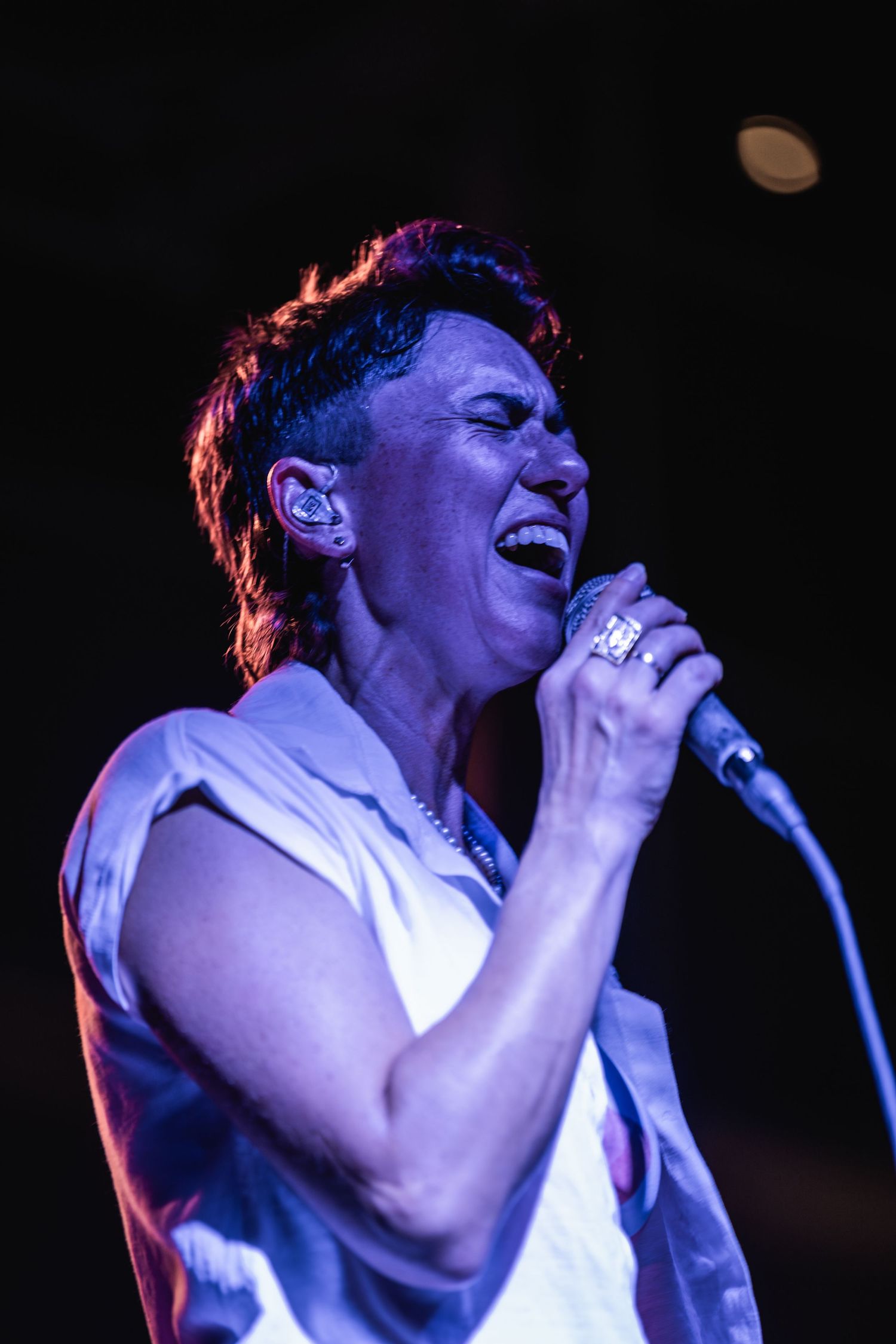 Concert performer singing passionately into microphone with dramatic blue and red stage lighting.