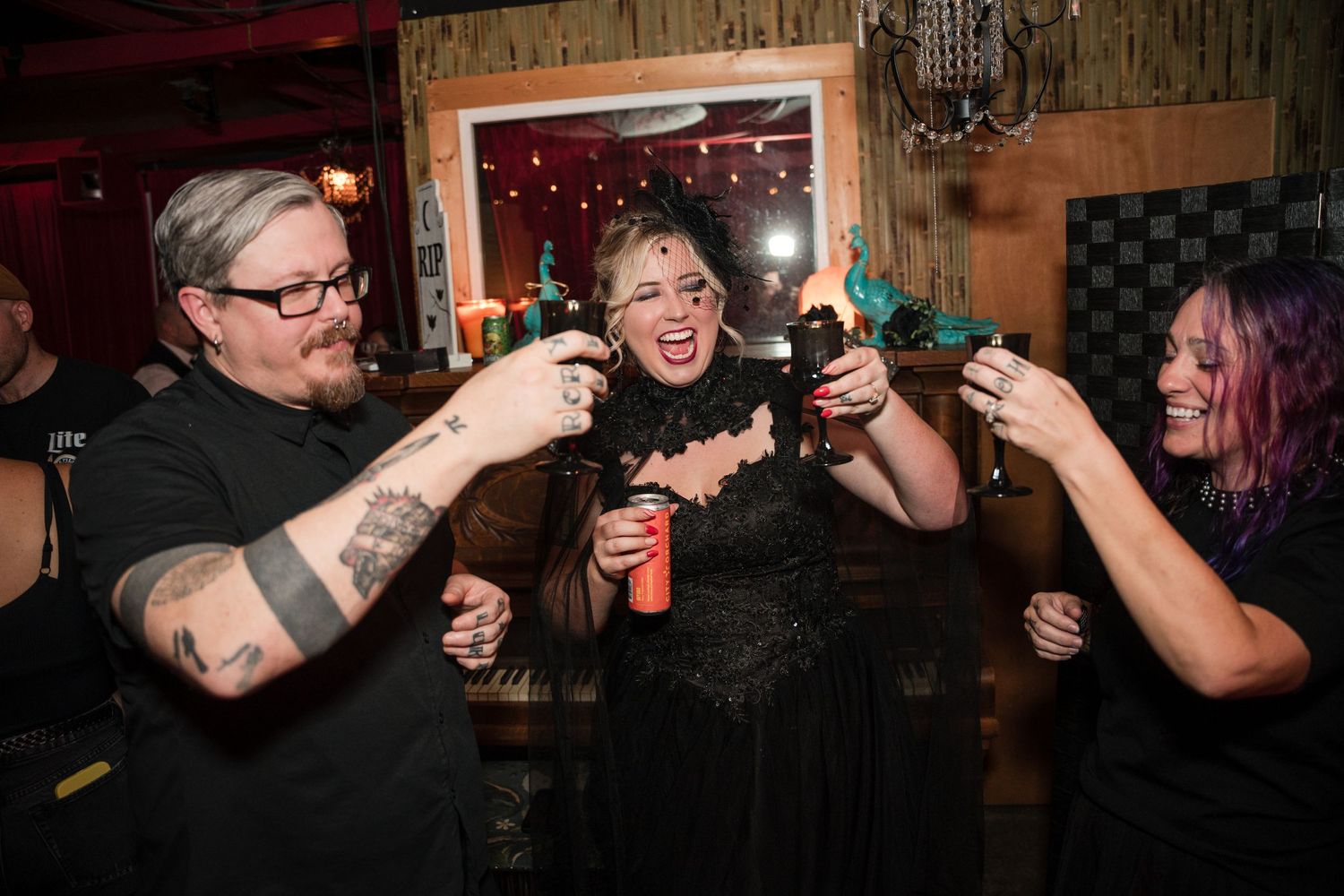 Friends toasting with drinks at a lively party with red ambient lighting.
