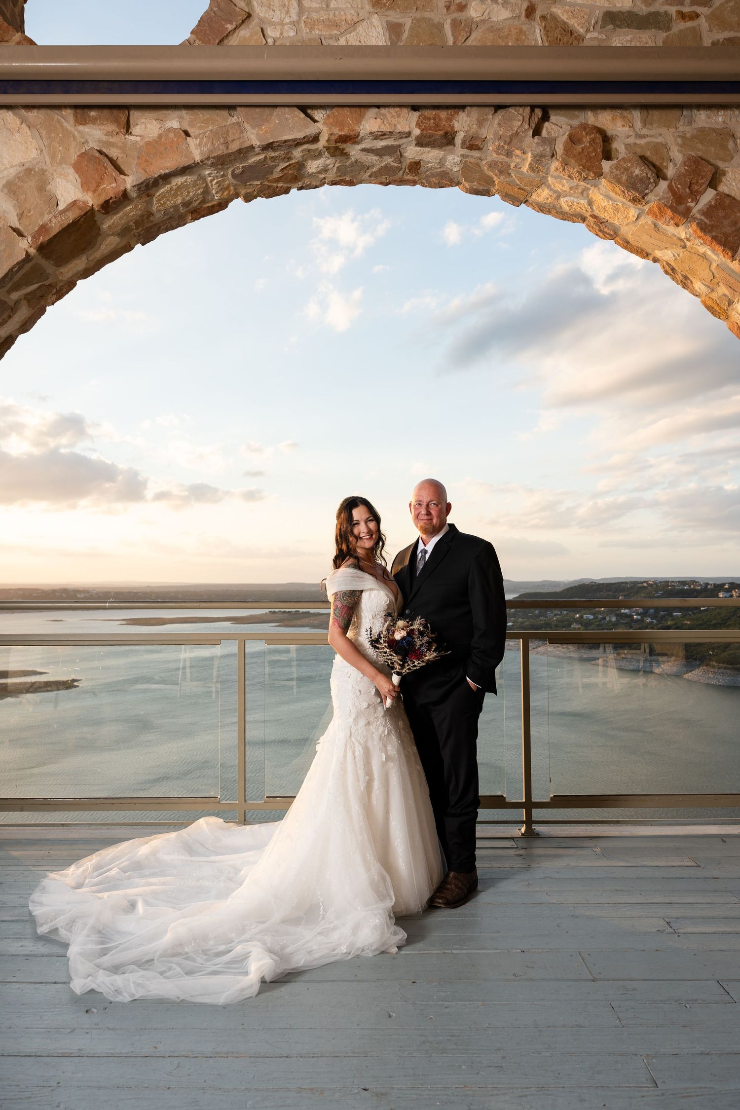 Sunset wedding portrait on a scenic balcony with stone arch and ocean view.