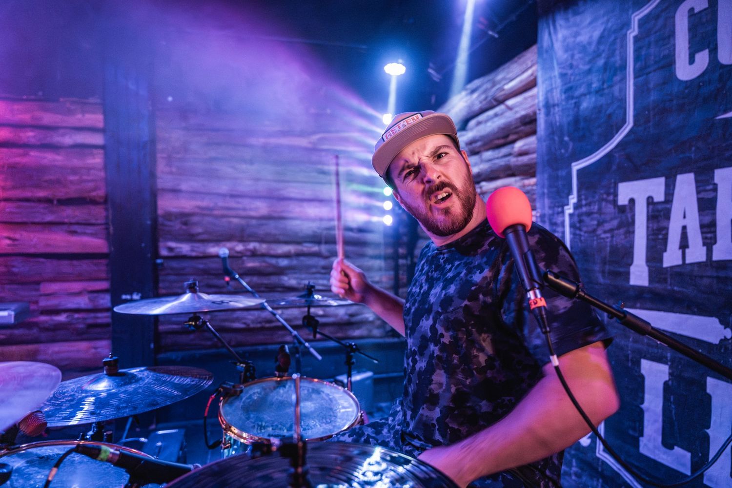 Energetic drummer performing with colorful purple stage lighting.