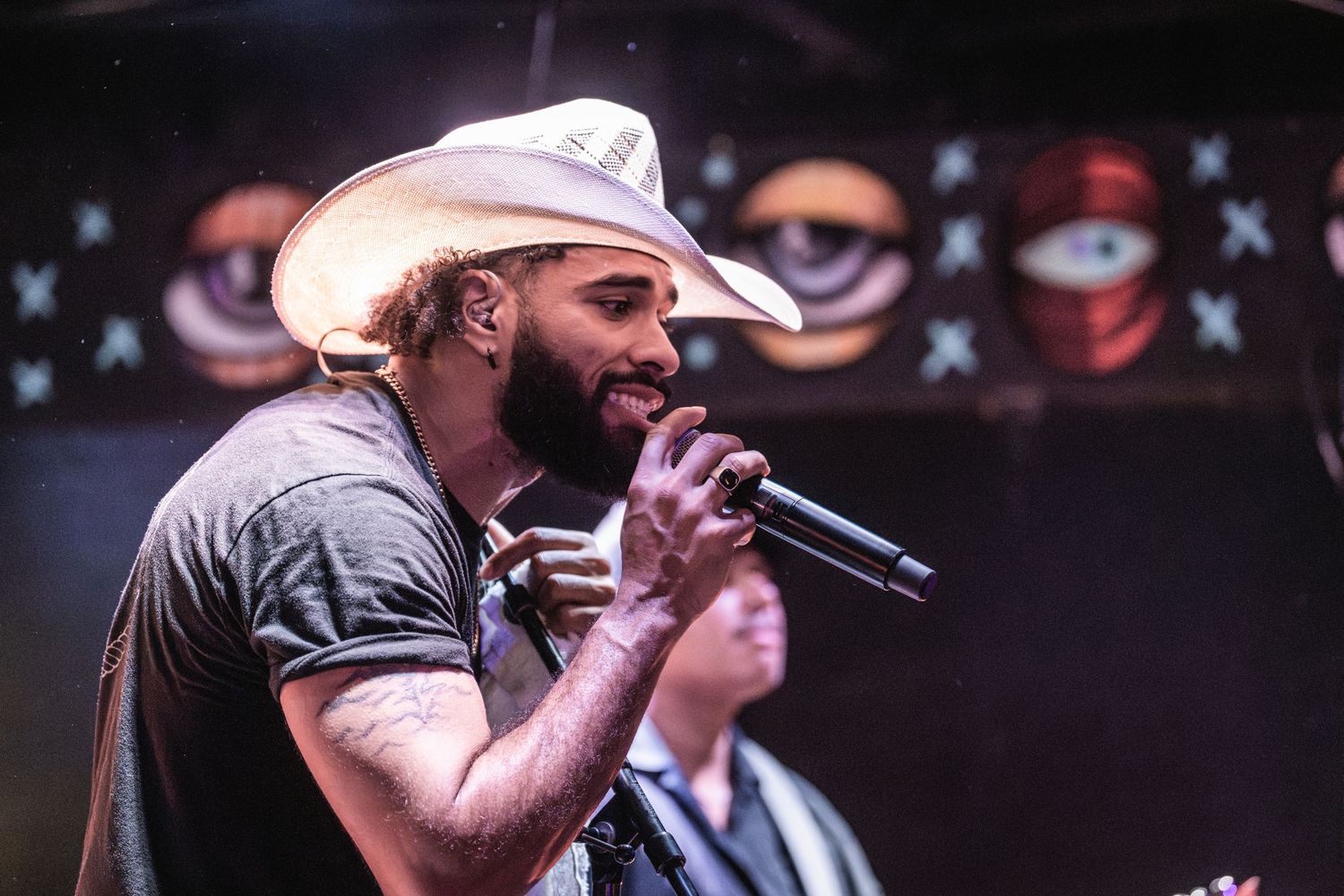 Country music performer singing energetically on stage with cowboy hat and microphone in dark lighting.