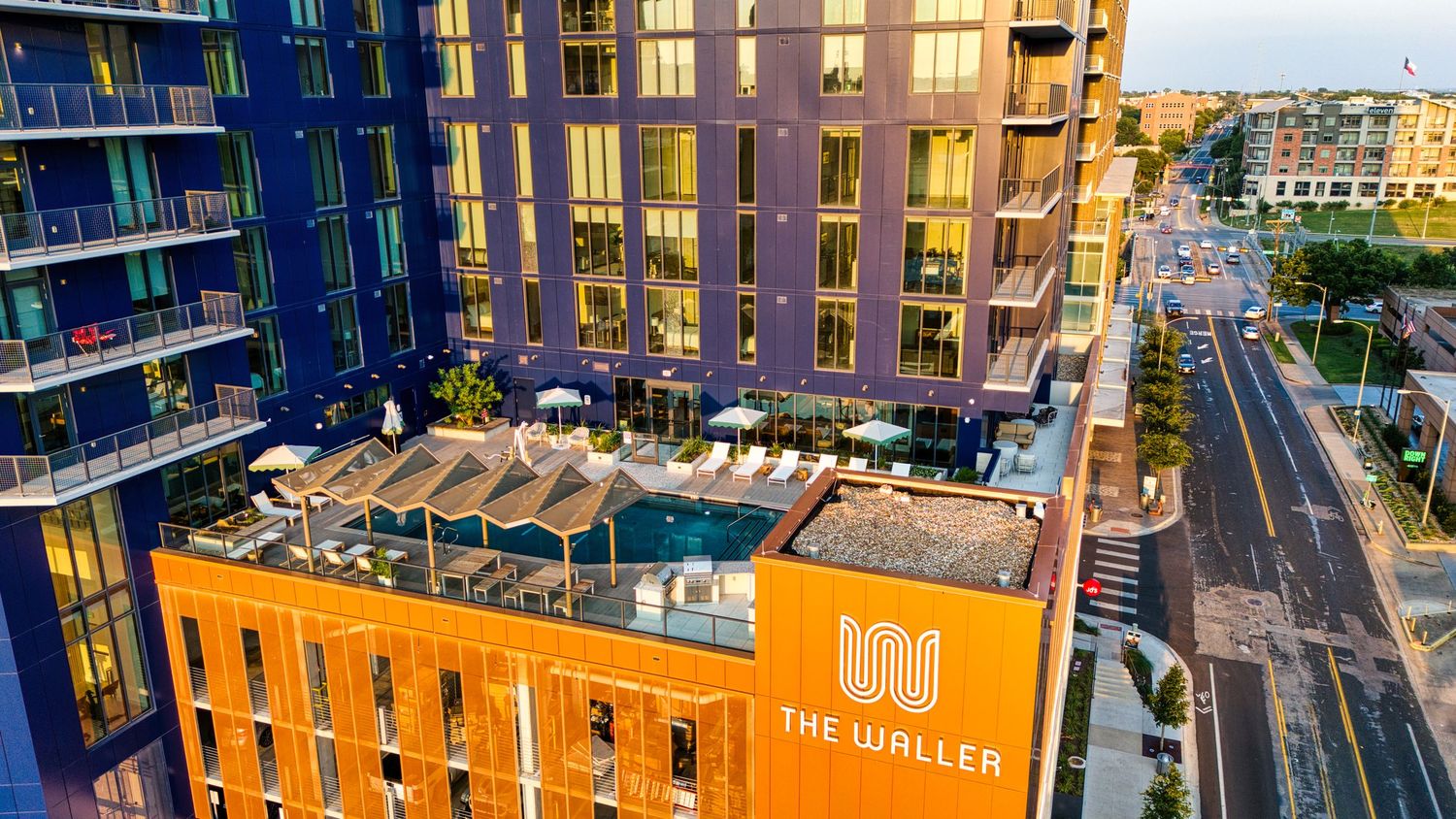 Aerial view of The Waller apartments featuring rooftop pool deck and orange architectural accents.