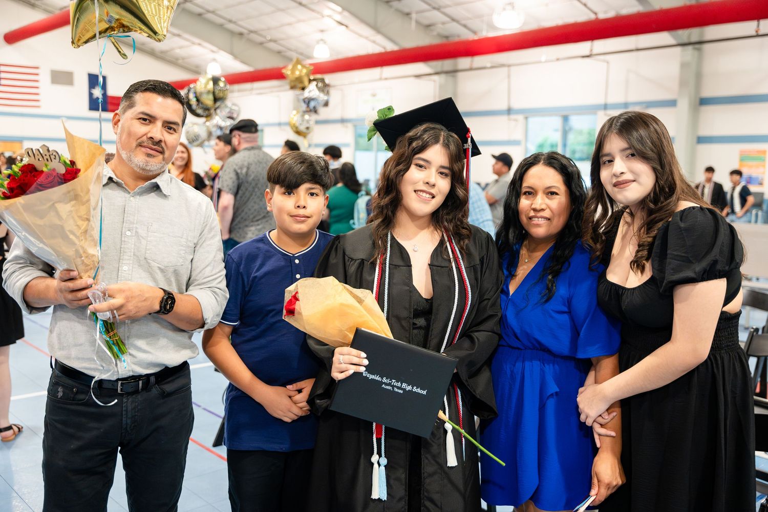 A group gathers indoors to celebrate a graduation ceremony with diplomas and festive decorations.