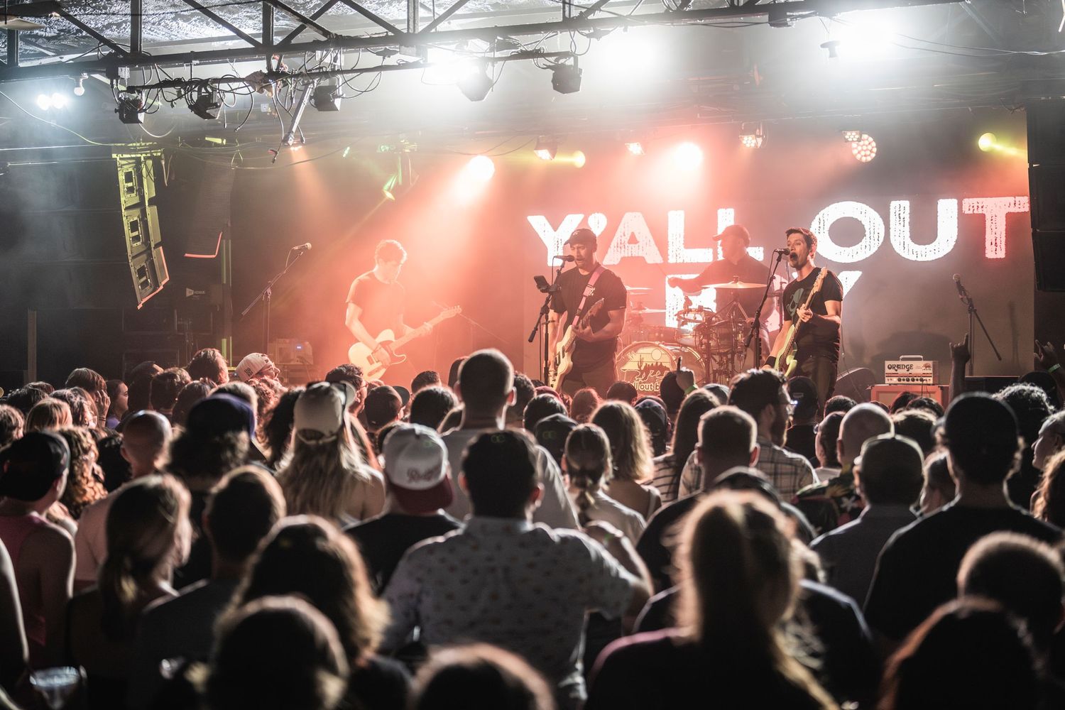 A crowd watches a live band perform on stage with bright red lighting and 