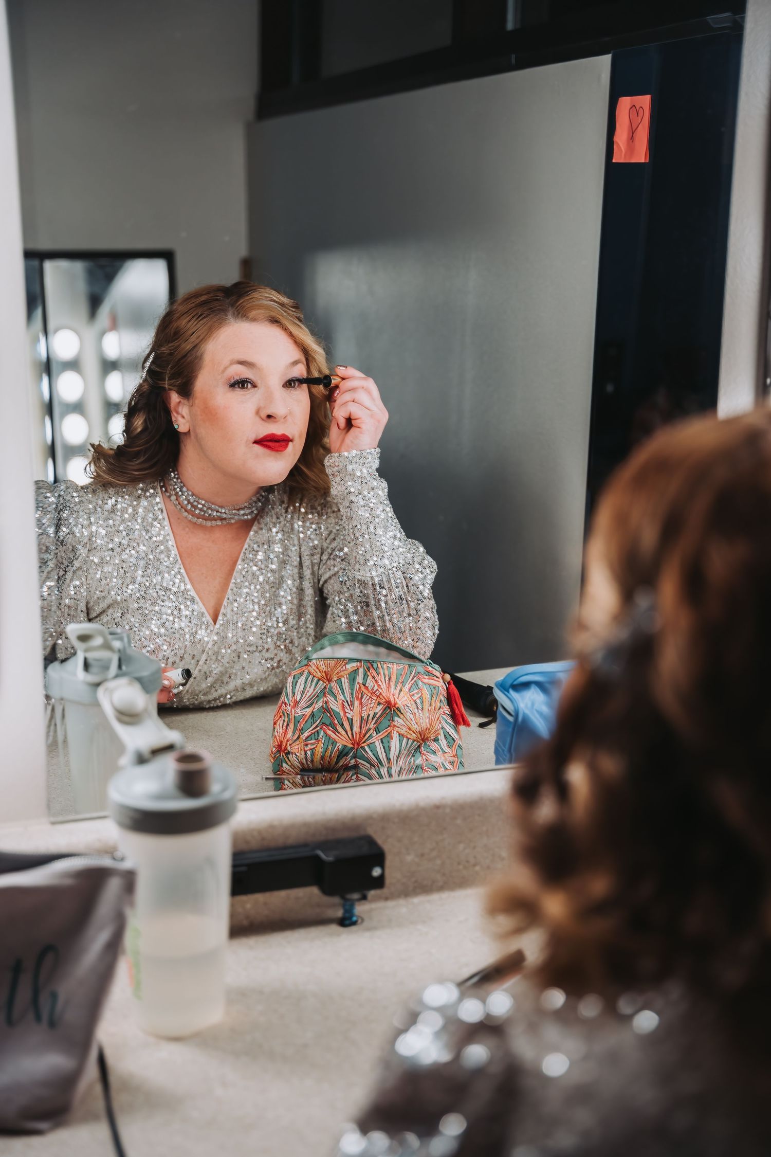 Performer in a sparkly silver dress getting ready in a dressing room mirror.