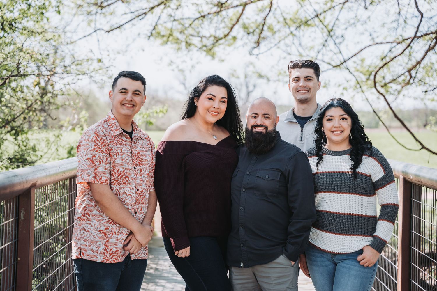 Group photo of five people standing together on a wooden bridge surrounded by spring foliage.