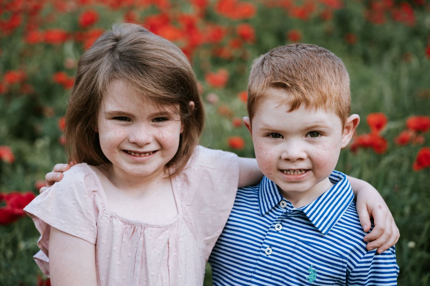 Two children pose together in front of a field of bright red poppies.