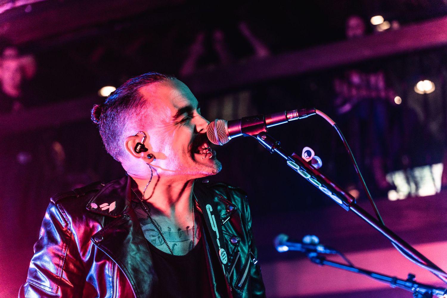 Musical performer illuminated by vibrant pink and blue stage lights while singing into microphone.