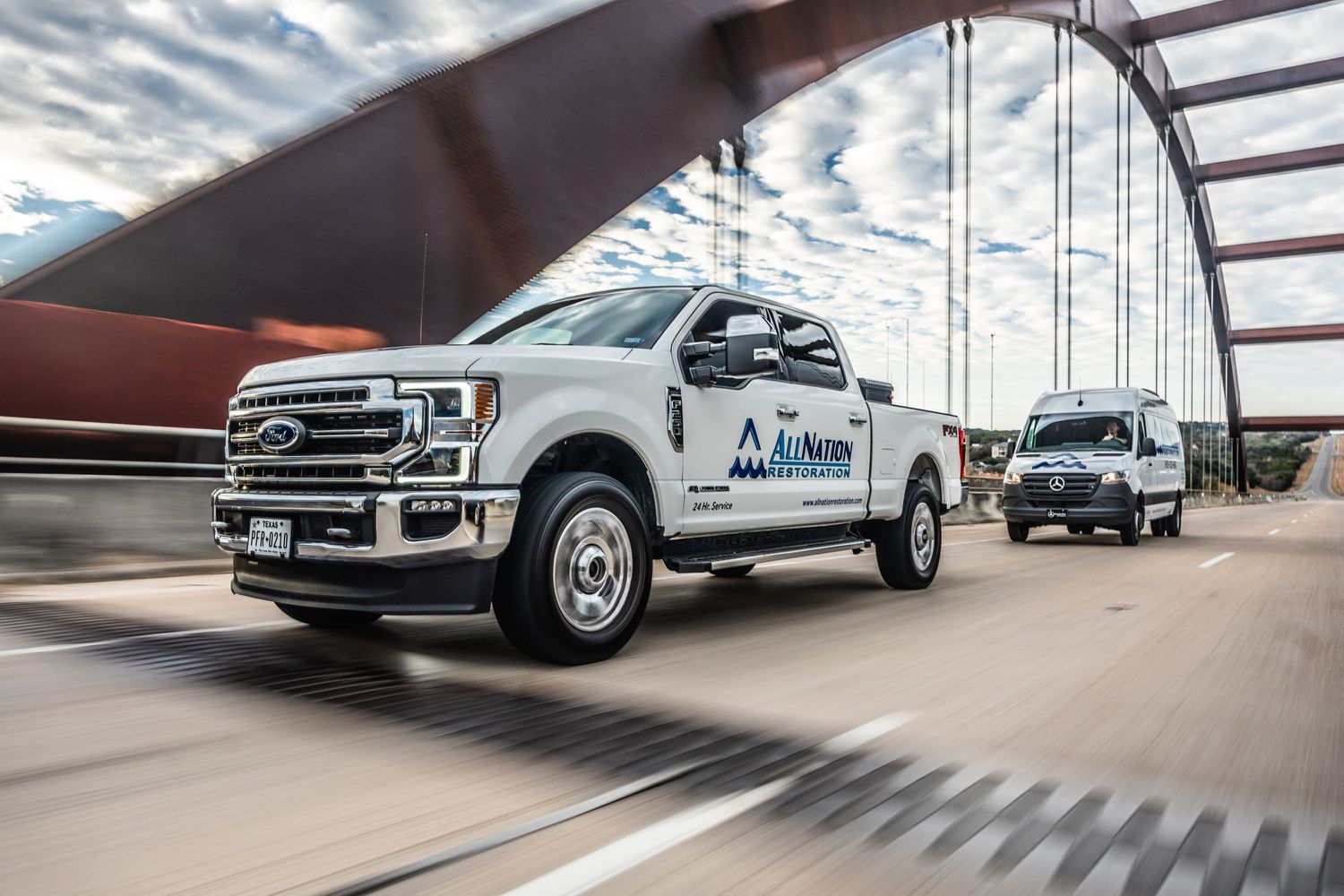 White Ford pickup truck with AirNow branding driving across a bridge under dramatic clouds.