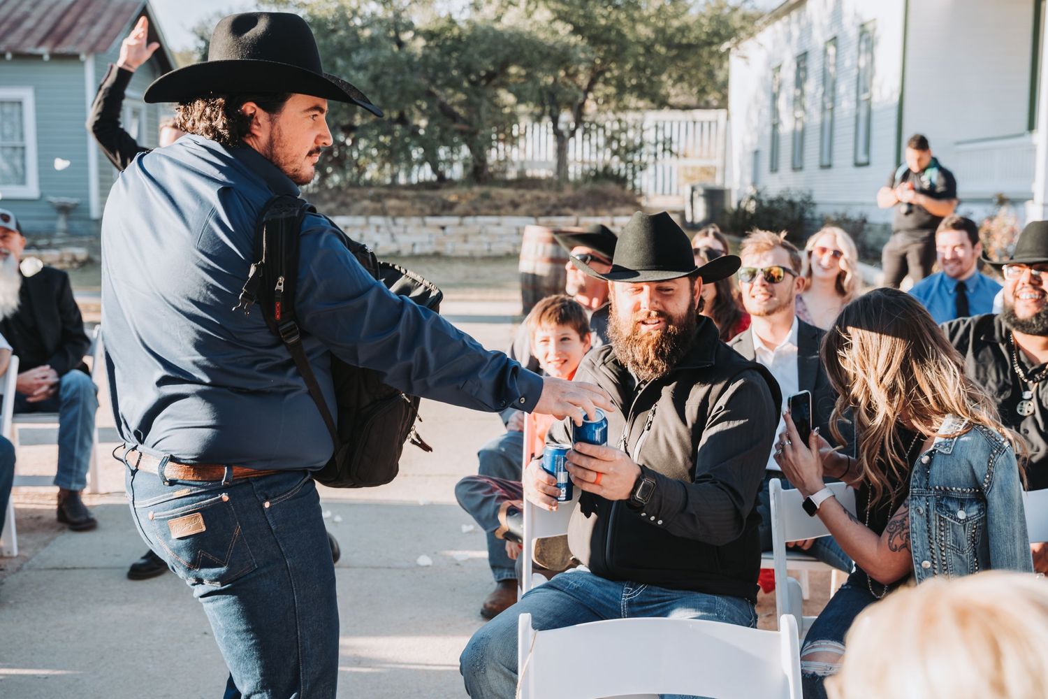 An animated performer in western attire entertains a seated outdoor audience.
