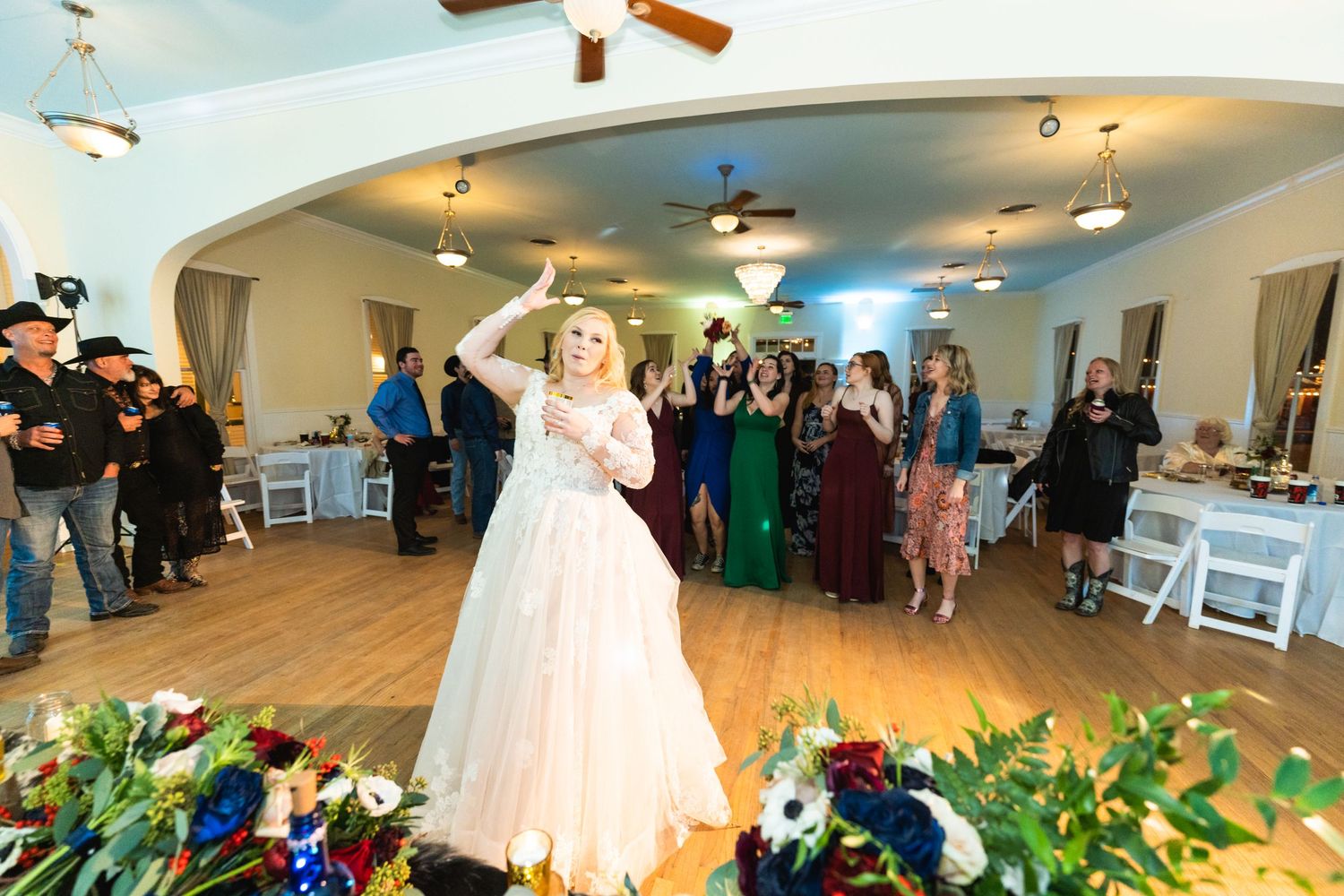 A bride in a white ballgown twirls on the dance floor surrounded by flowers and guests.