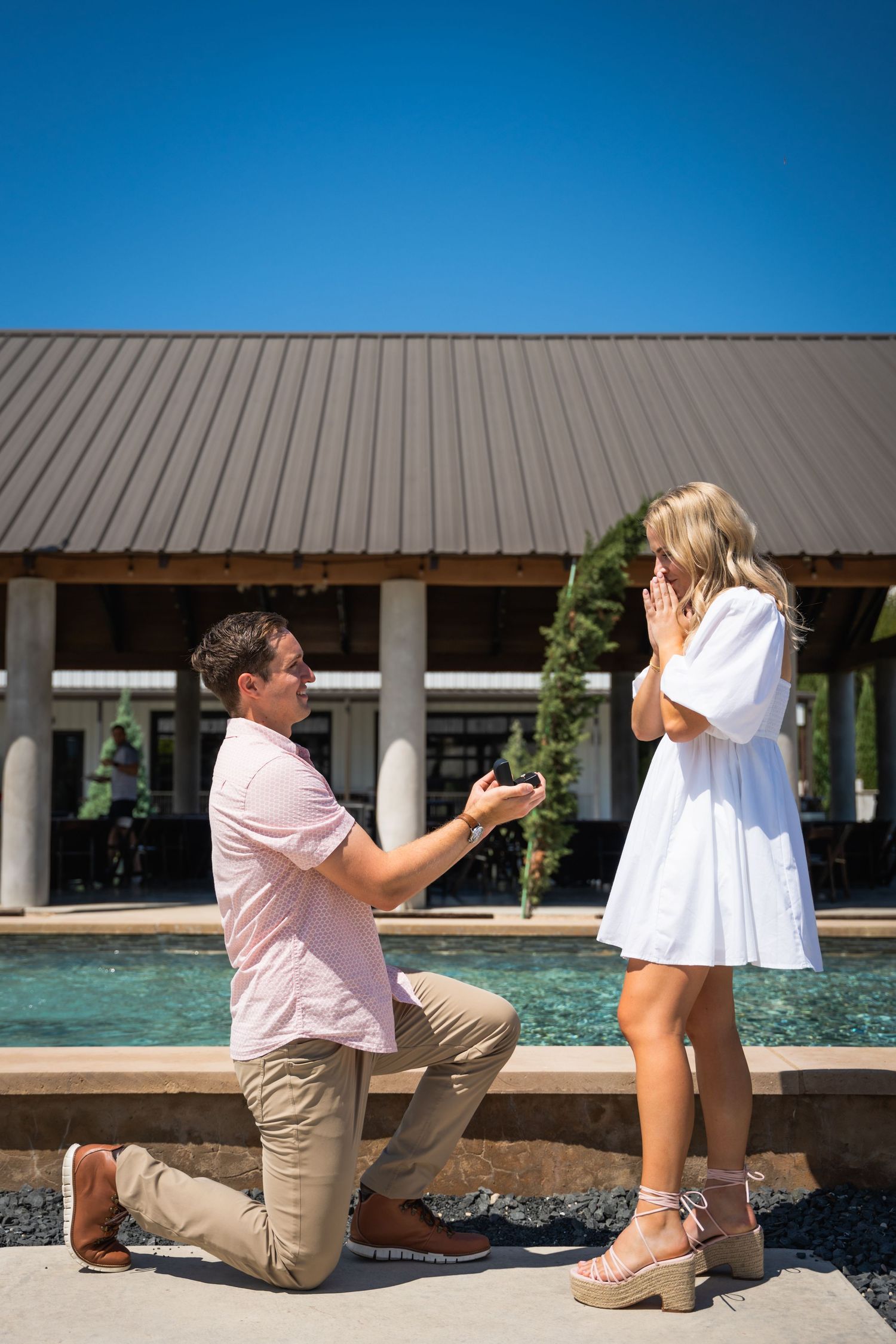 A surprise proposal moment captured poolside with a modern pavilion in the background.