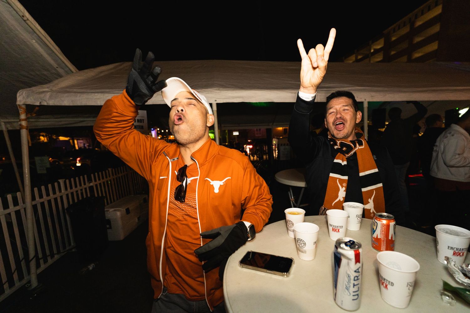 People making rock hand gestures while celebrating at an outdoor table.