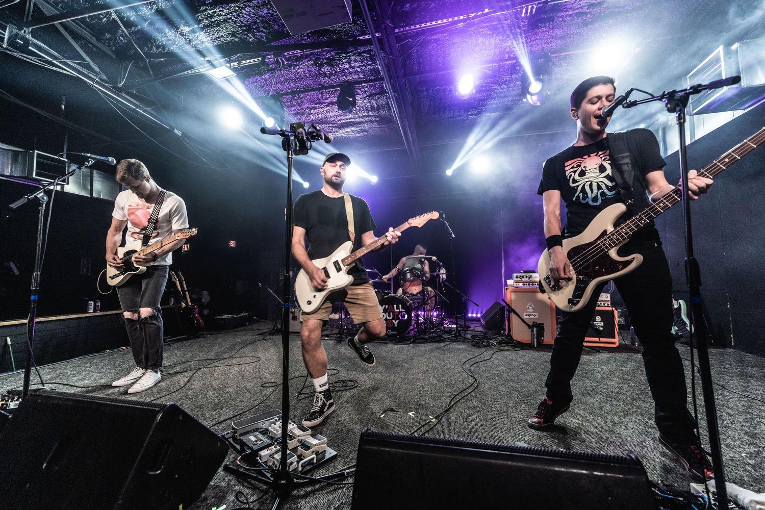 Wide angle shot of rock band members playing guitars on illuminated concert stage.