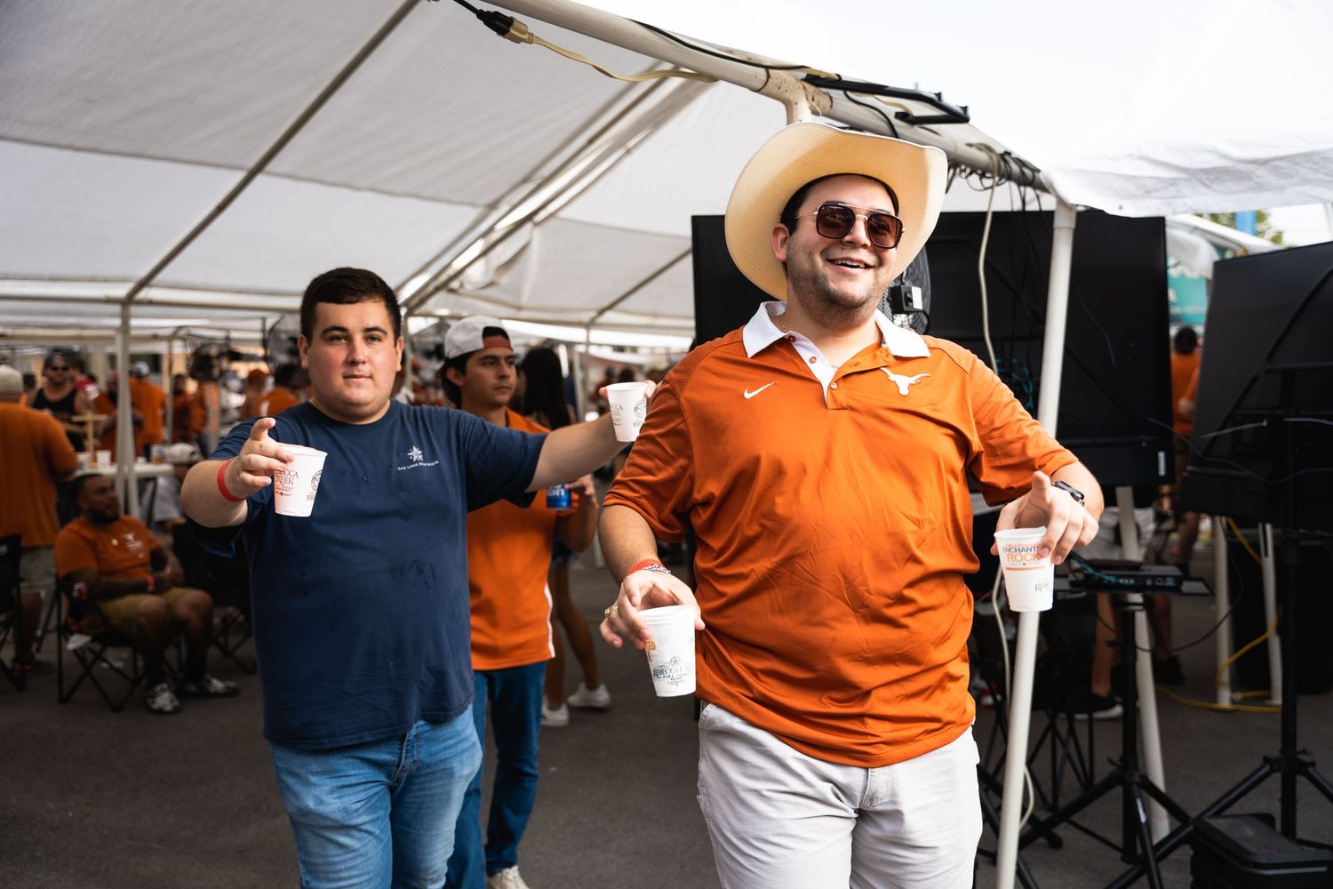 Two attendees enjoying drinks at outdoor party under white tent canopy.