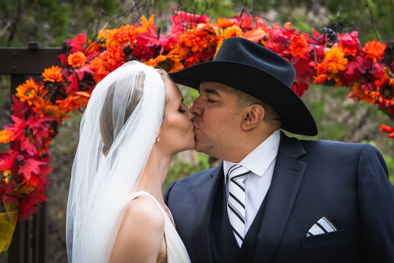 Newlywed couple sharing a kiss under an arch of vibrant red and orange flowers.