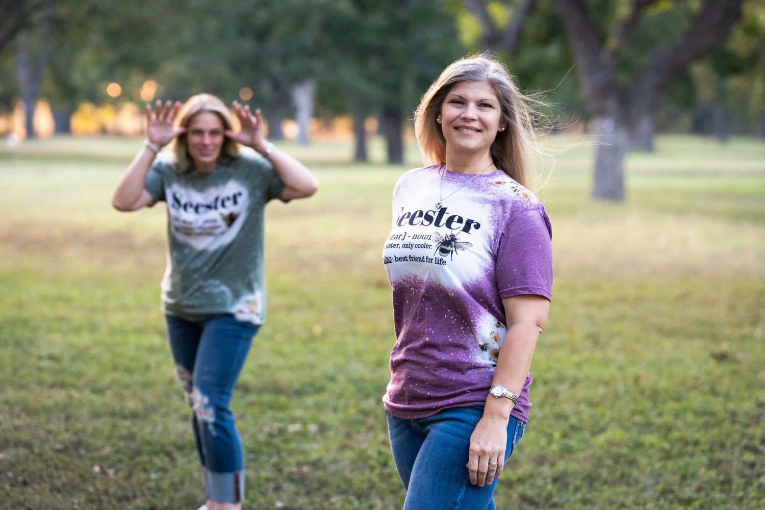 Two people in coordinated shirts play and pose while running through a park.