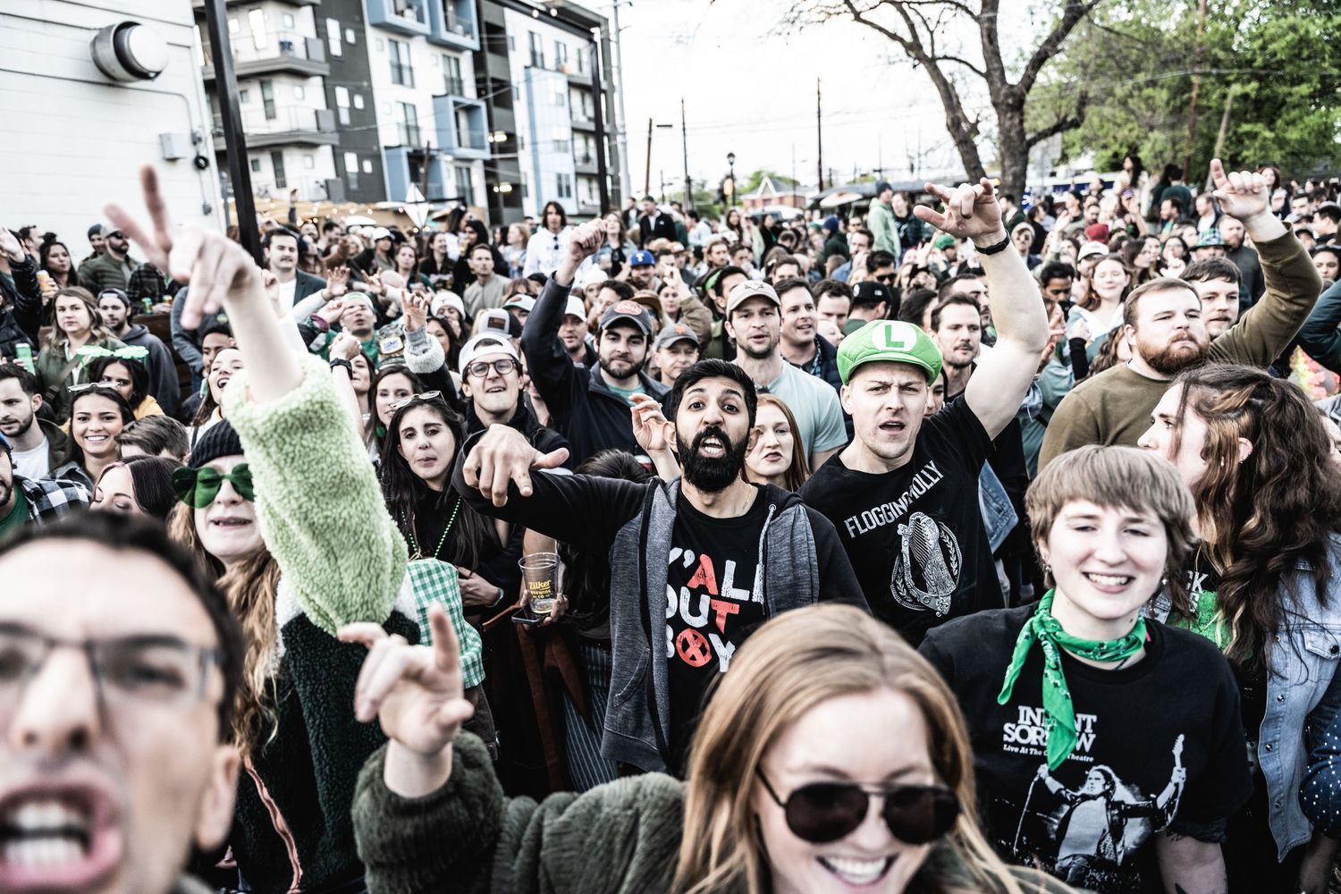Large crowd cheering with raised hands at outdoor music festival.