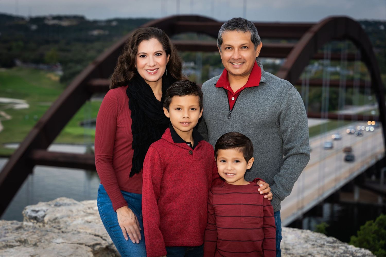Family portrait with coordinated red and grey outfits in front of Pennybacker Bridge.