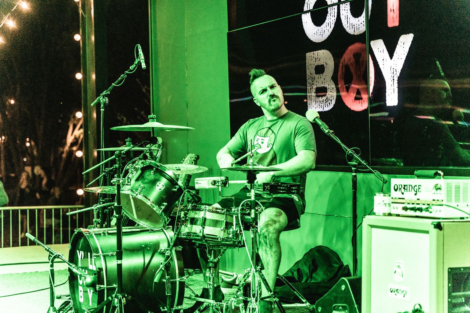 Drummer performs on stage with green lighting and 'BOY' text visible in background.