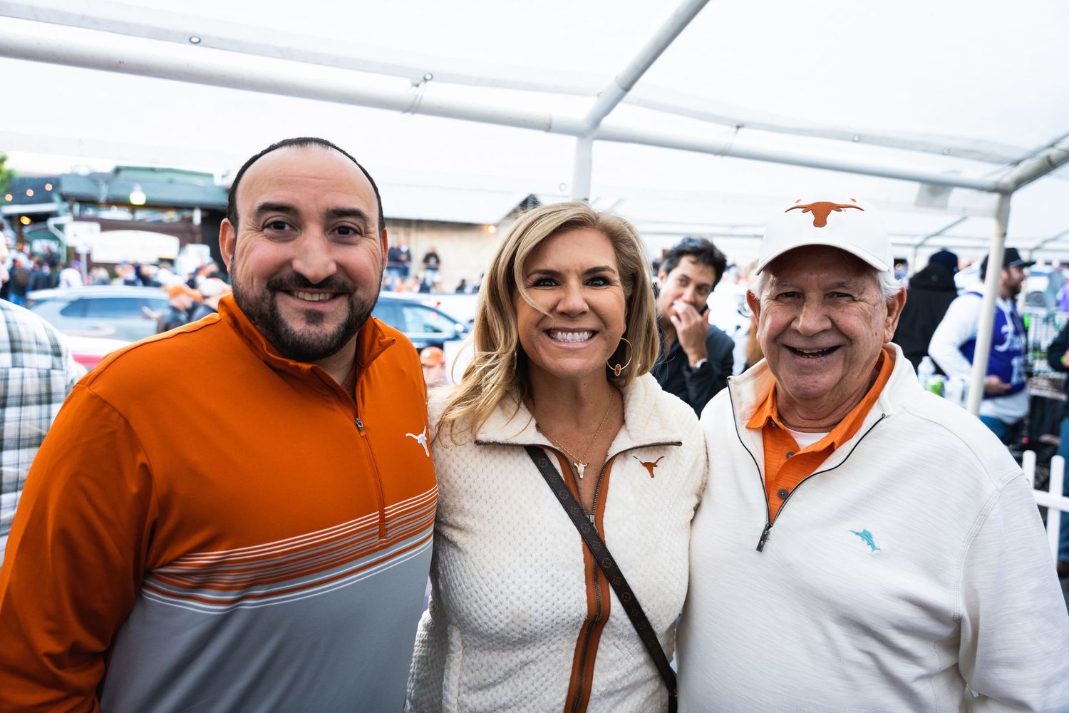 Three people in orange and white clothing pose together at an outdoor party.