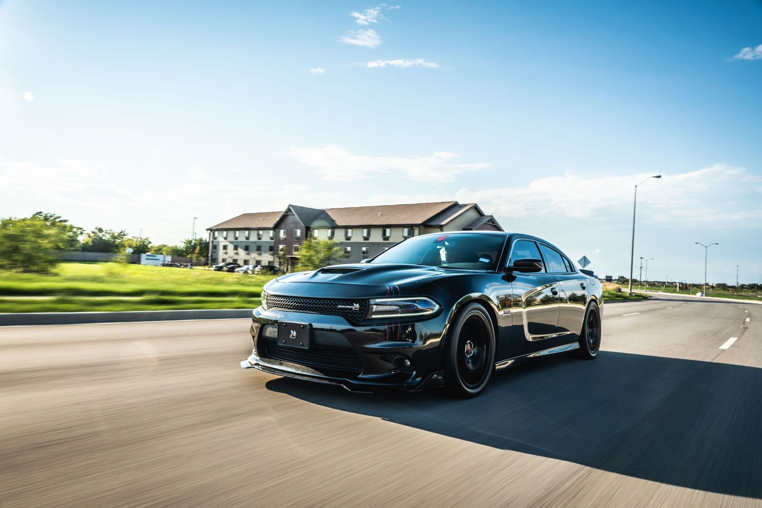 Modified black Dodge Charger with custom wheels cruising on suburban road.