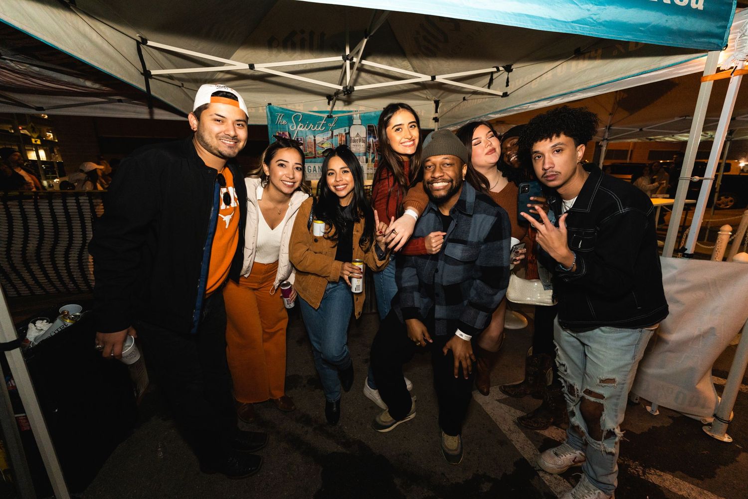 Group of friends posing together under a tent at a nighttime outdoor event.