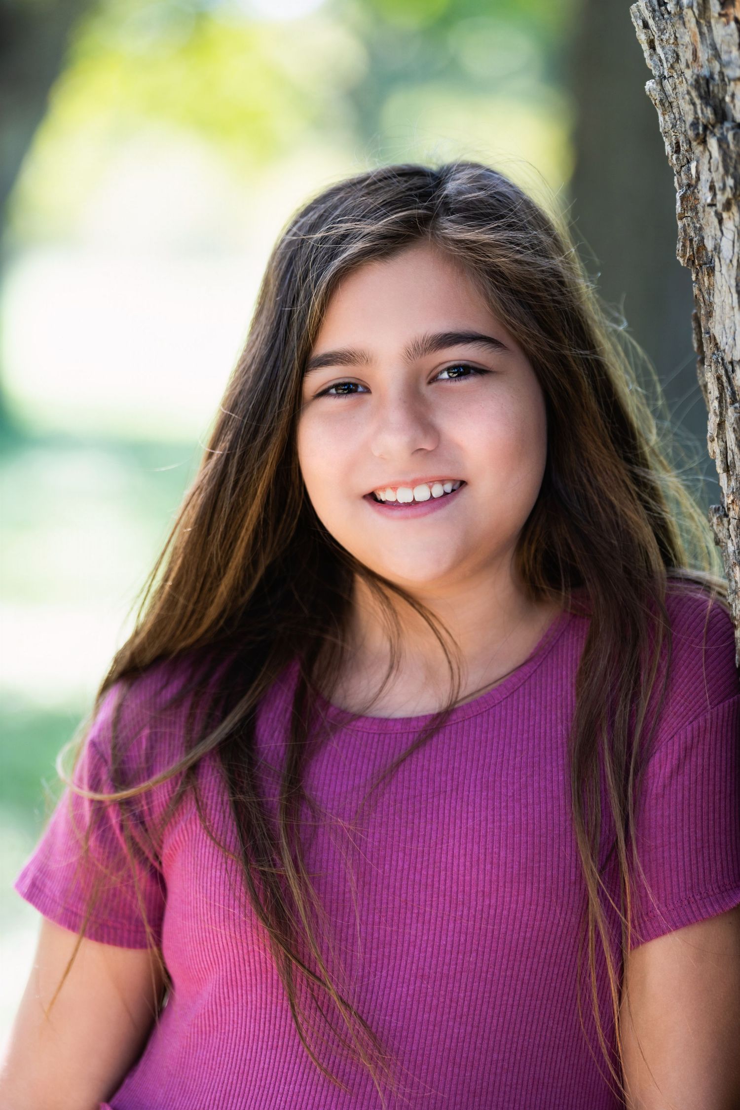 Natural light portrait with soft bokeh background featuring purple top and long brown hair.