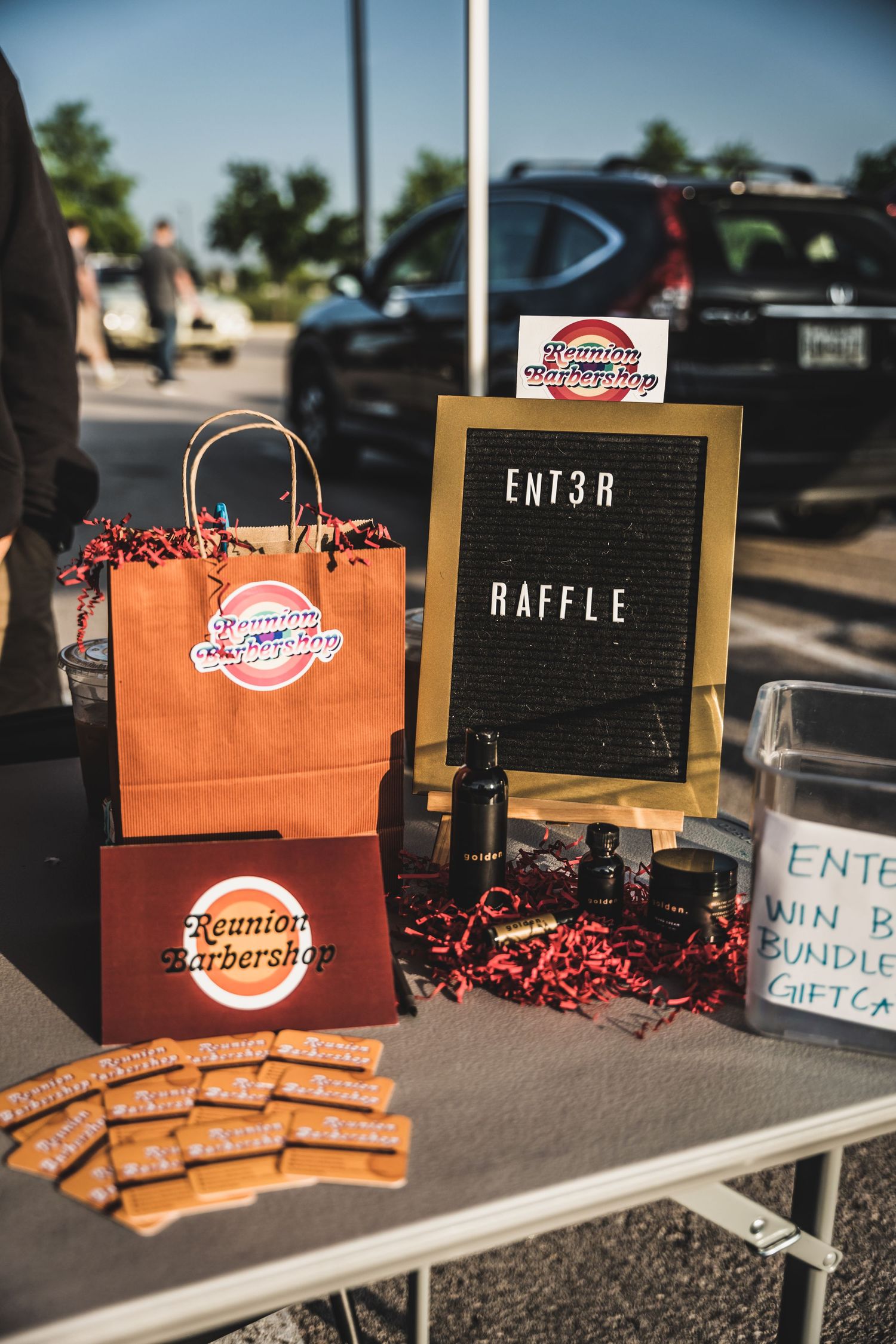 A promotional display table with orange gift bags, a raffle sign, and marketing materials at an outdoor event.