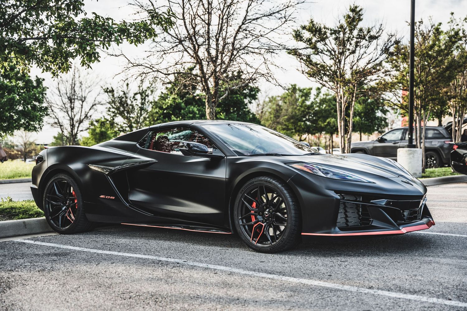 Black Chevrolet Corvette sports car with red accents parked in outdoor lot.