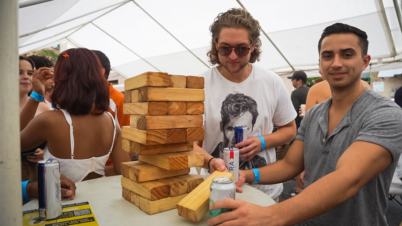 Group playing giant Jenga game under white tent at outdoor festival.