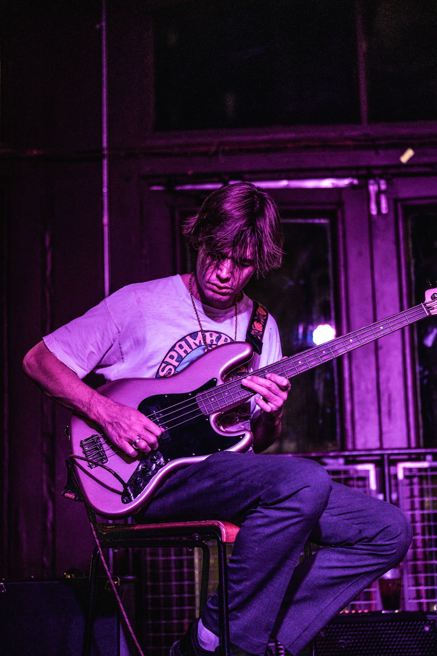 Bass player in purple lighting performs seated while intensely focused on instrument.