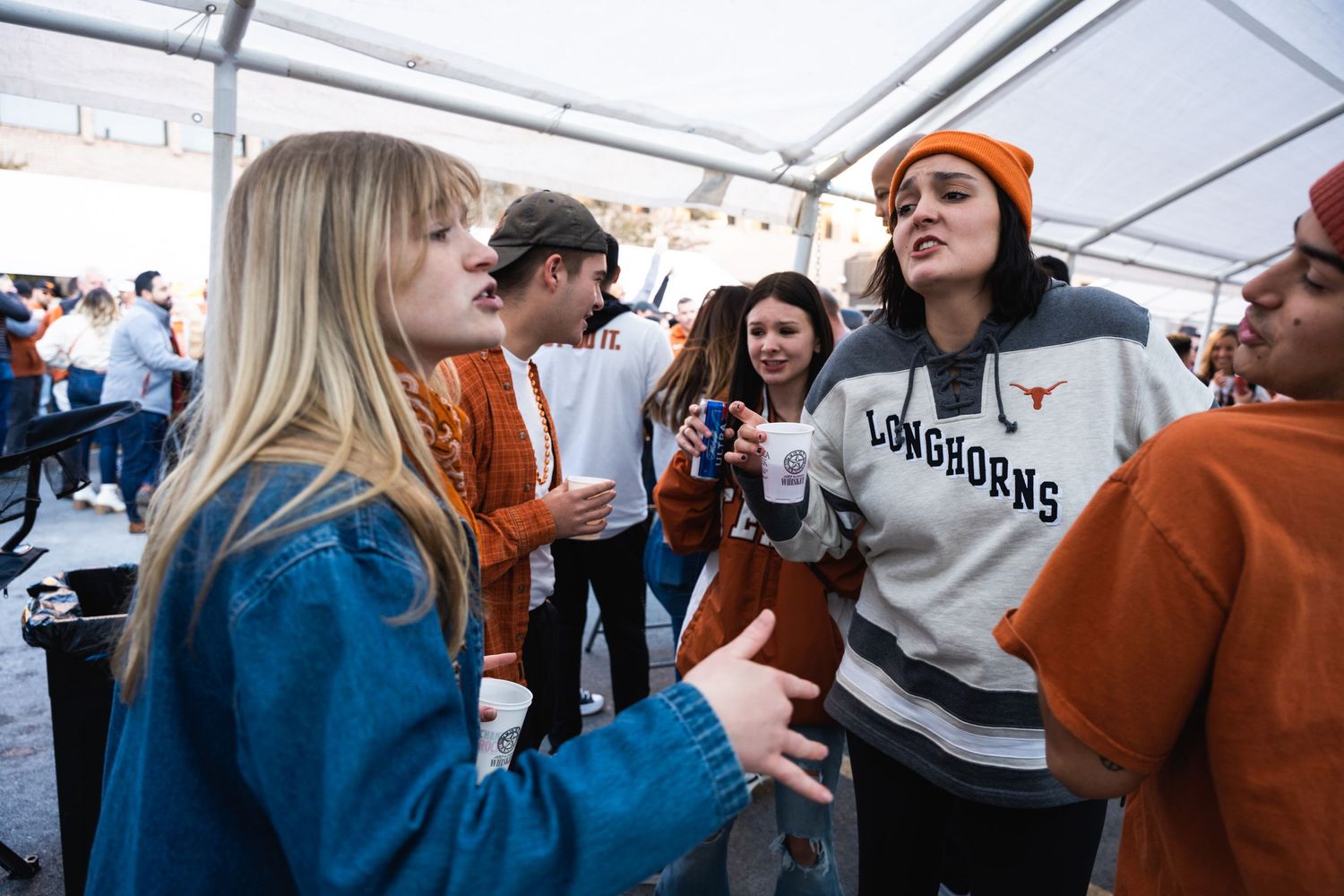 Group engaged in animated conversation at outdoor event wearing orange and blue.