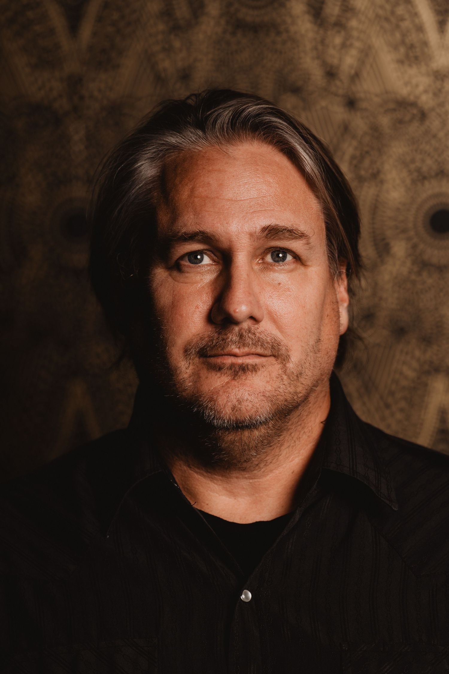 Warm-toned portrait of a man in black shirt against textured brown background.