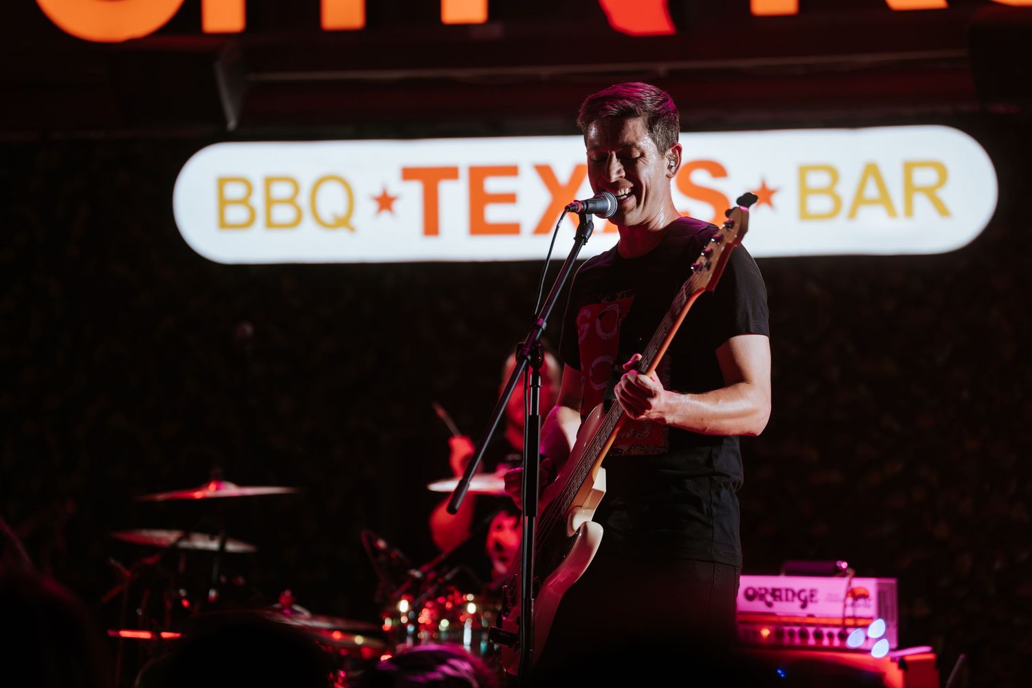 Musician performs on stage at BBQ Texas Bar with red lighting and neon signage.