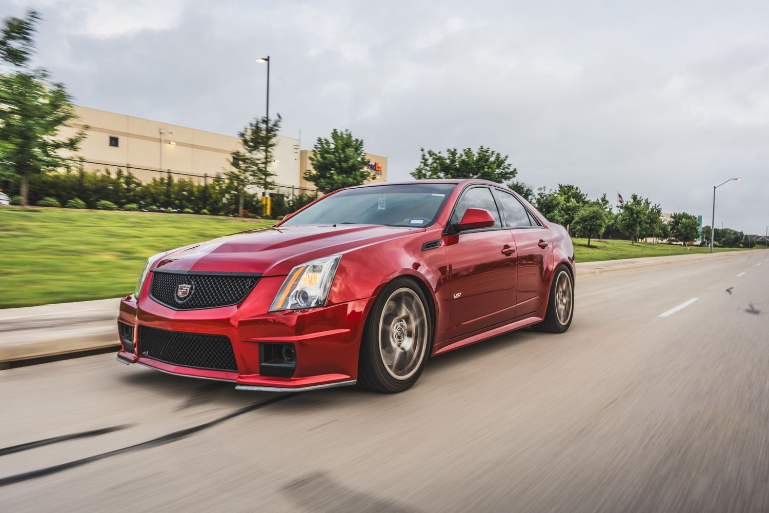 Red Cadillac CTS-V sport sedan with performance wheels cruising on suburban road.