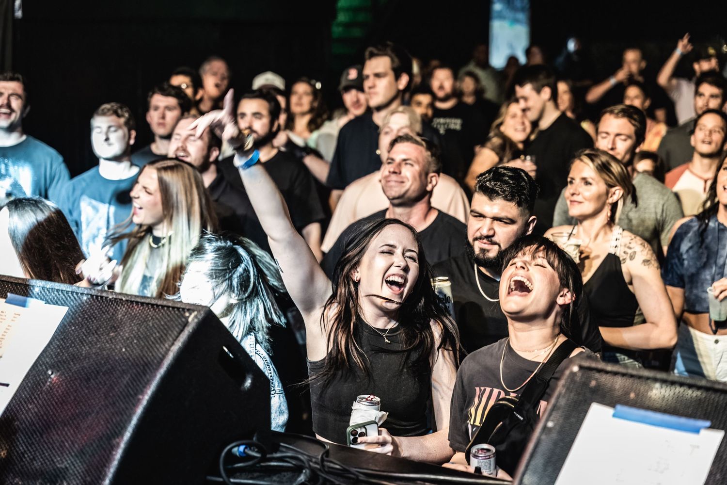 Enthusiastic crowd of concert-goers singing and cheering at live music performance.