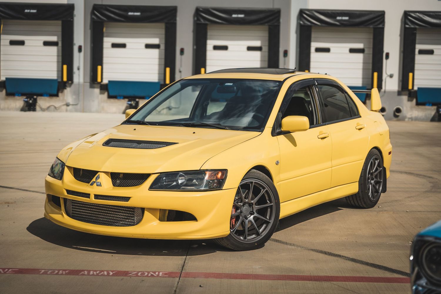 Yellow Mitsubishi Lancer Evolution with black wheels parked at loading dock.