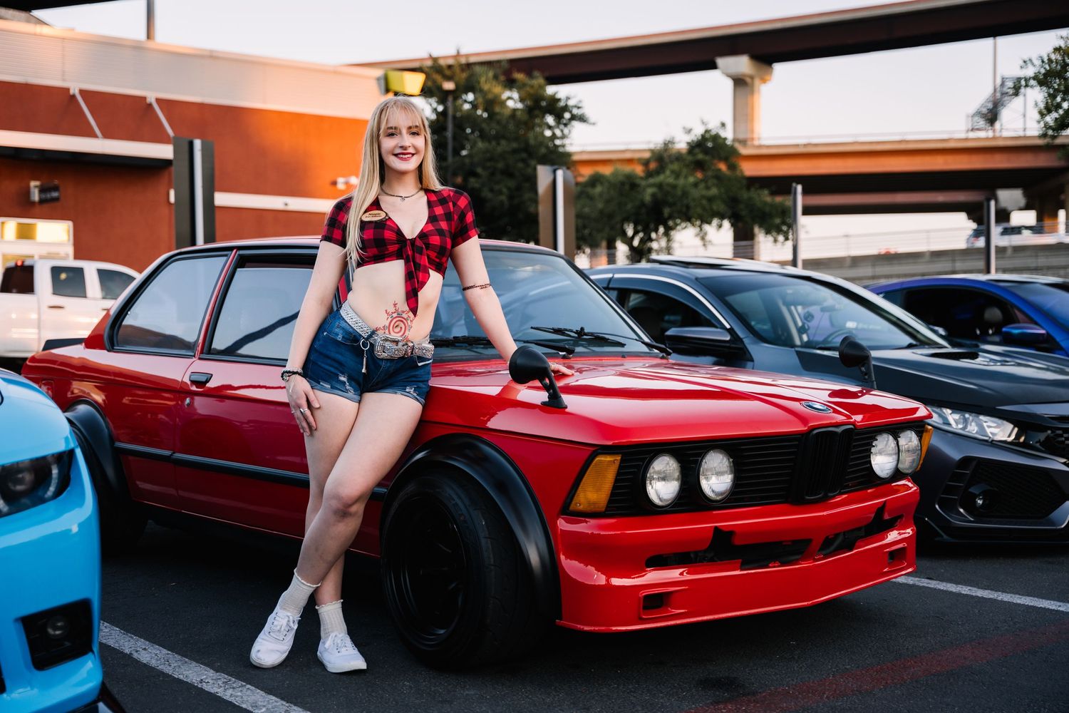 Red BMW E30 with custom modifications displayed at a car show.