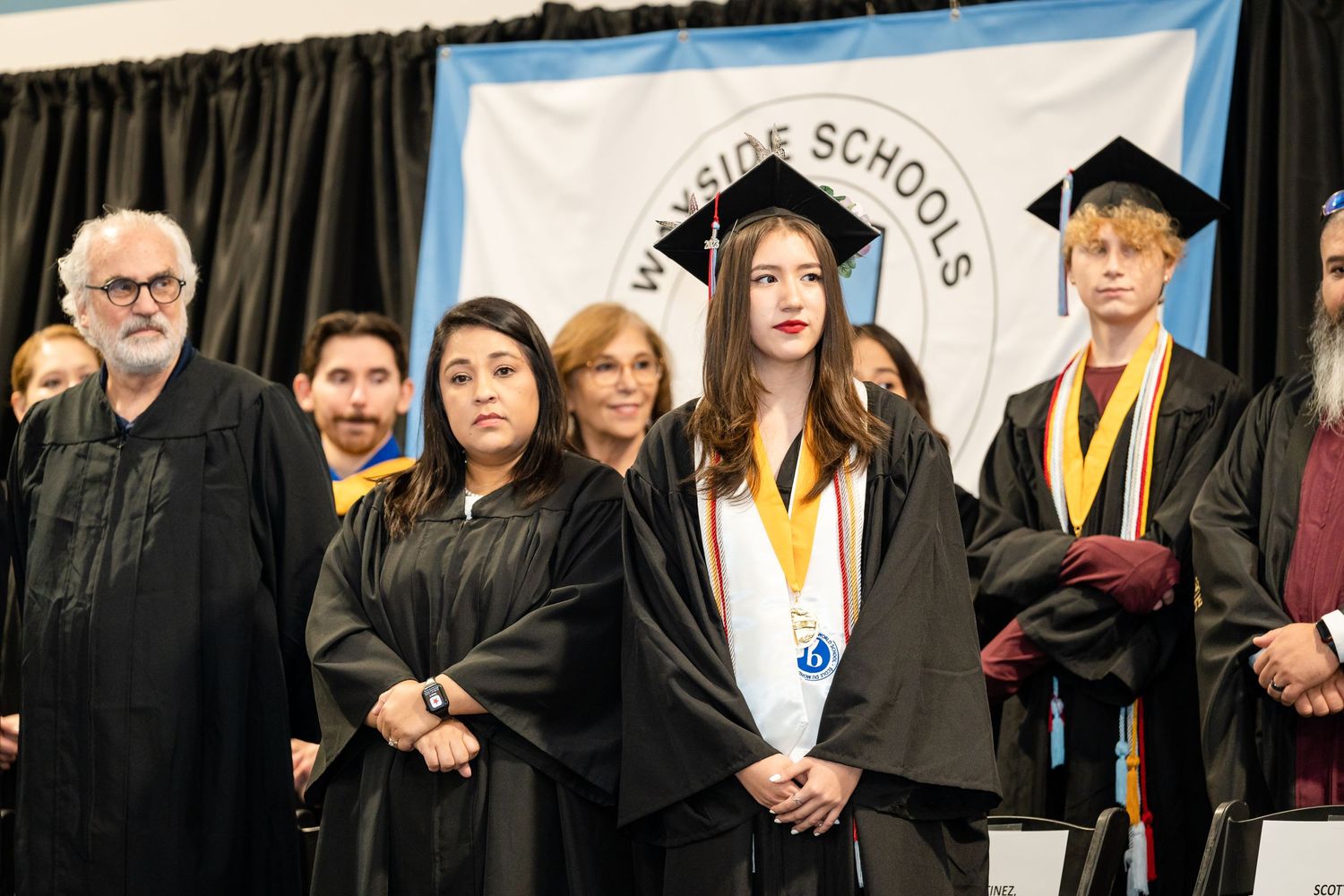 Graduates in traditional black academic regalia stand during a commencement ceremony.