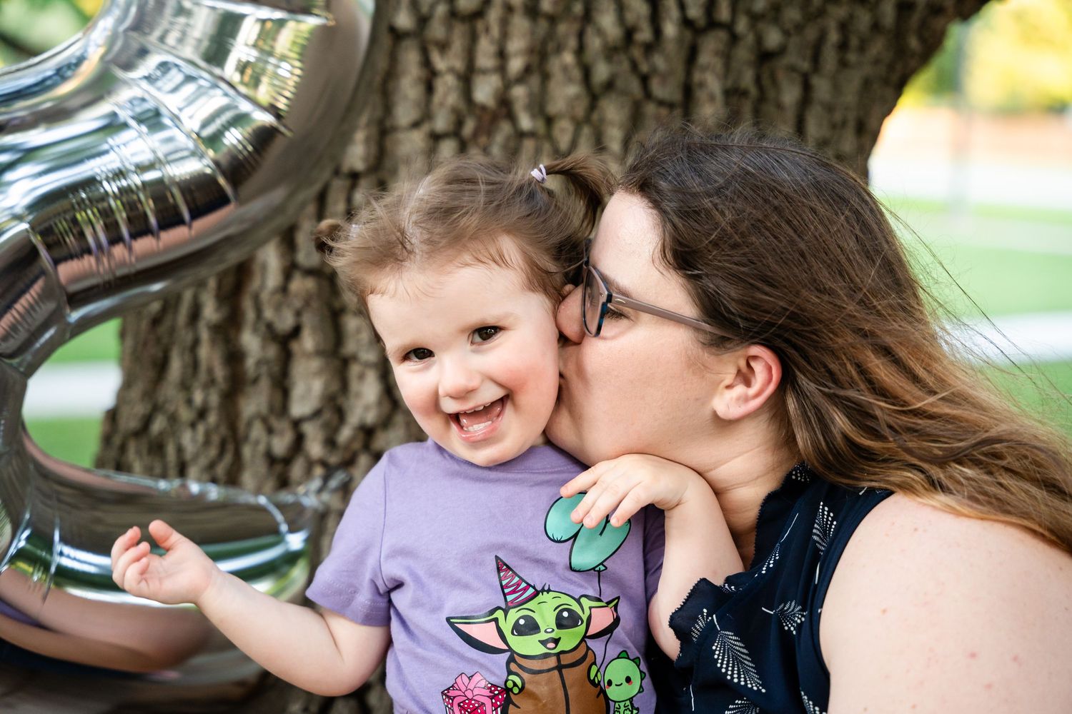 A joyful outdoor celebration with silver balloons and a large tree in the background.