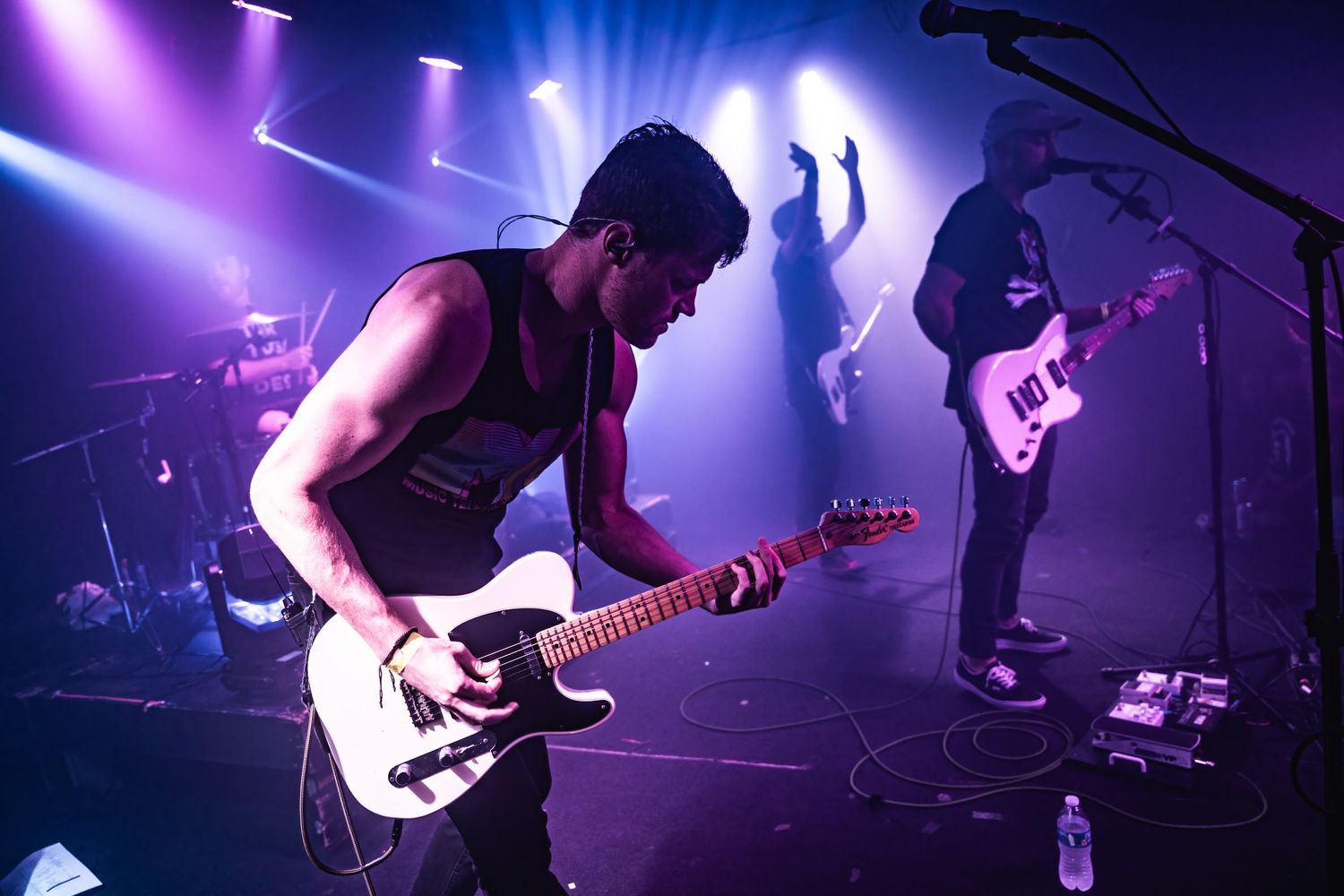 Rock band performing live on stage with dramatic purple and white lighting effects.