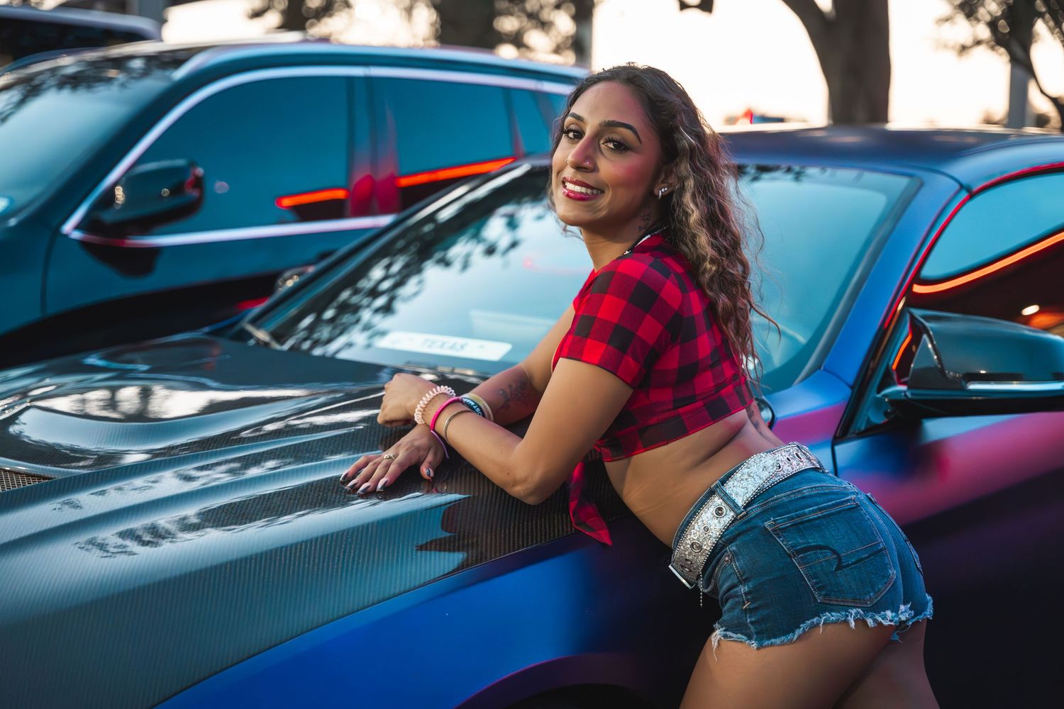 Red plaid crop top styled against performance cars at sunset.