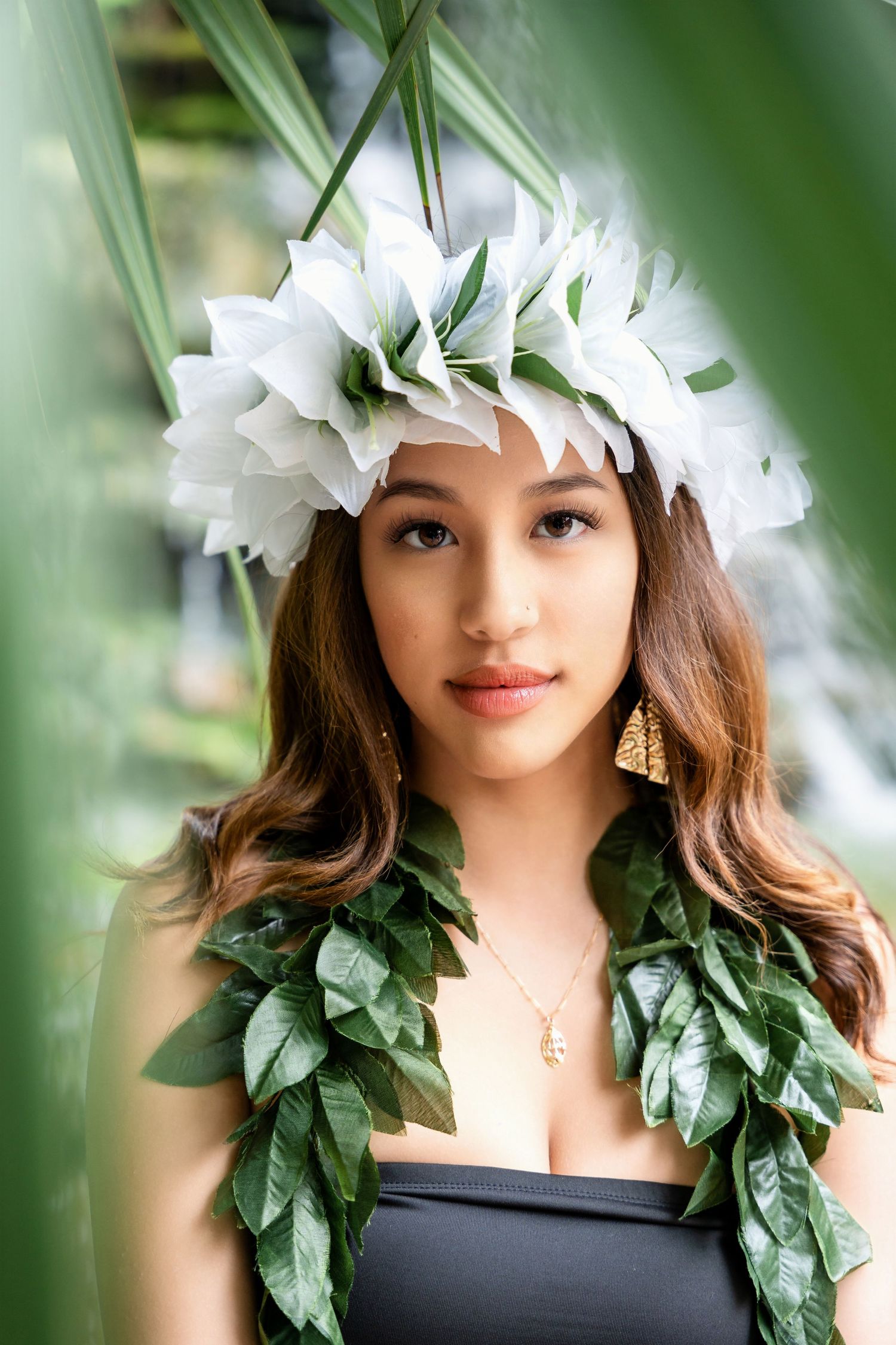 Close-up portrait with white flower crown and green leaf garland framed by tropical foliage.
